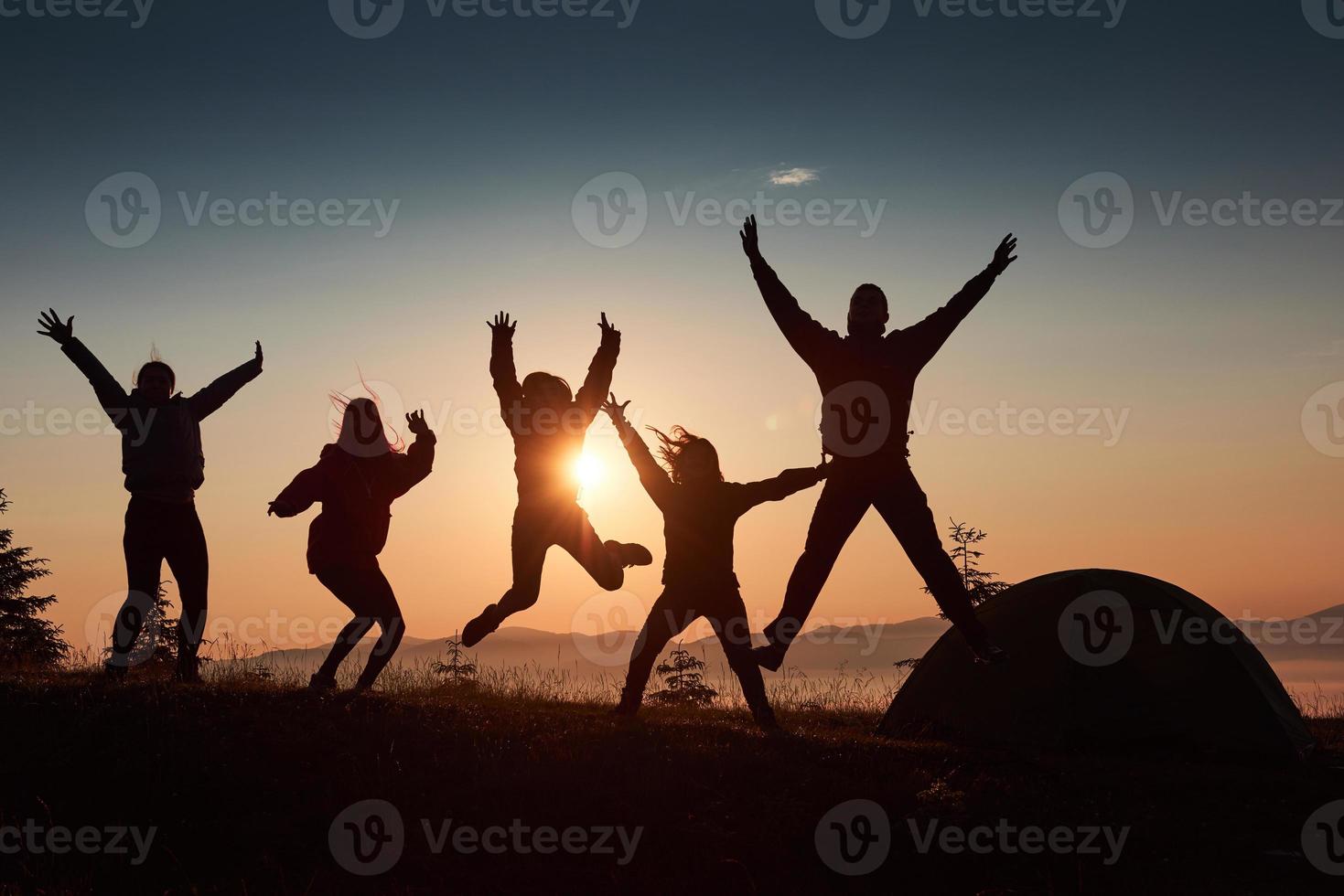 Una silueta de un grupo de personas se divierte en la cima de la montaña cerca de la carpa durante la puesta de sol. foto