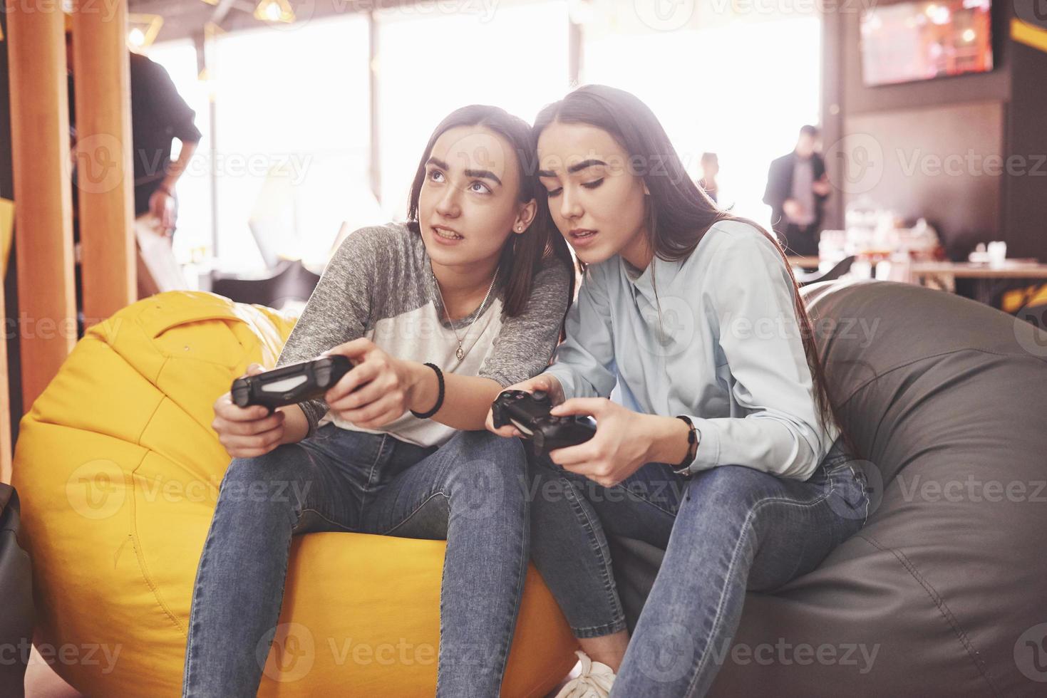 Twin sister sisters play on the console. Girls hold joysticks in their hands and have fun photo