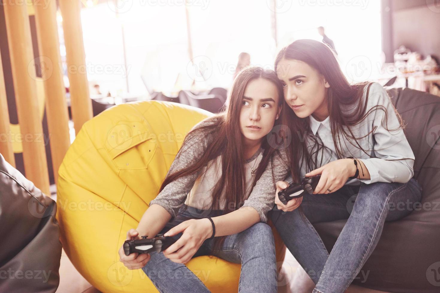 Twin sister sisters play on the console. Girls hold joysticks in their hands and have fun photo