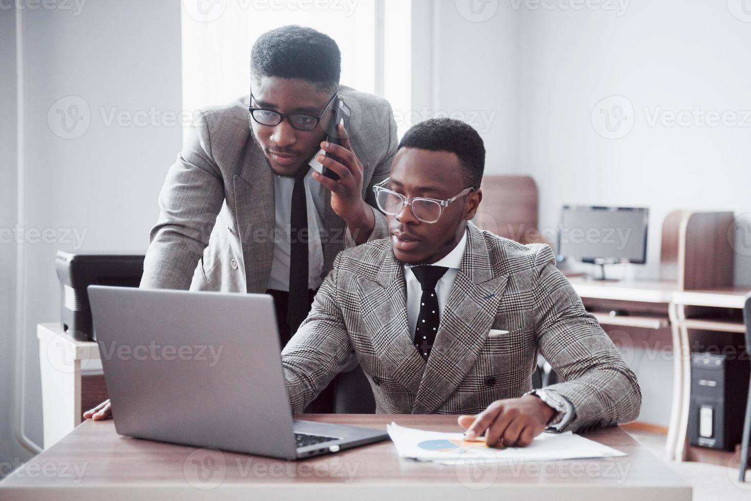 empresario moderno en el trabajo. Dos hombres de negocios confiados en ropa formal discutiendo algo y miran el monitor de la computadora portátil foto