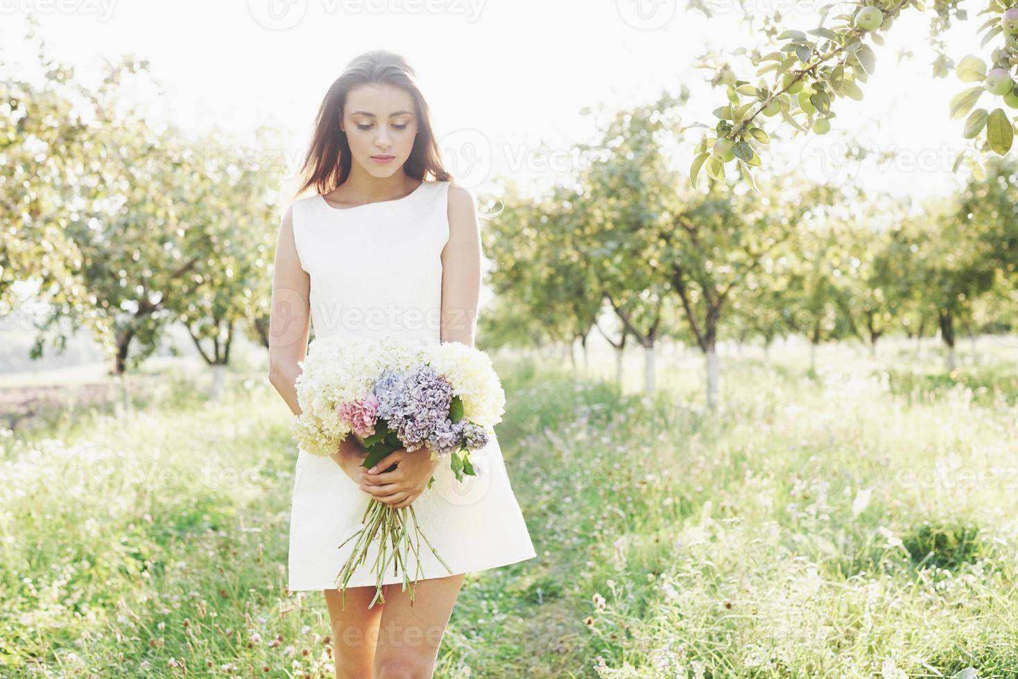 Beautiful young woman wearing elegant white dress and enjoying beautiful sunny afternoon in a summer garden photo