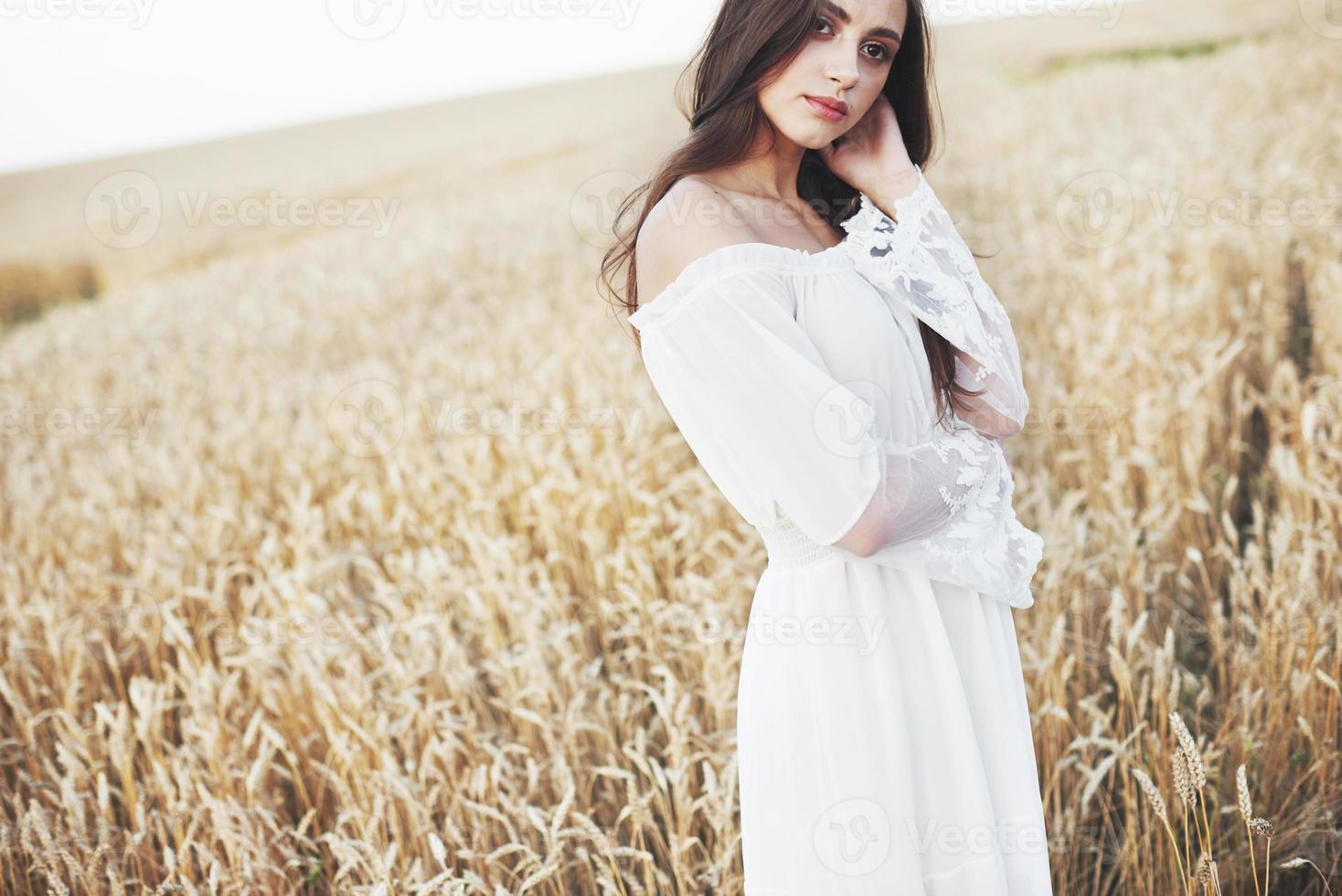 Sensible joven vestida de blanco posando en un campo de trigo dorado foto