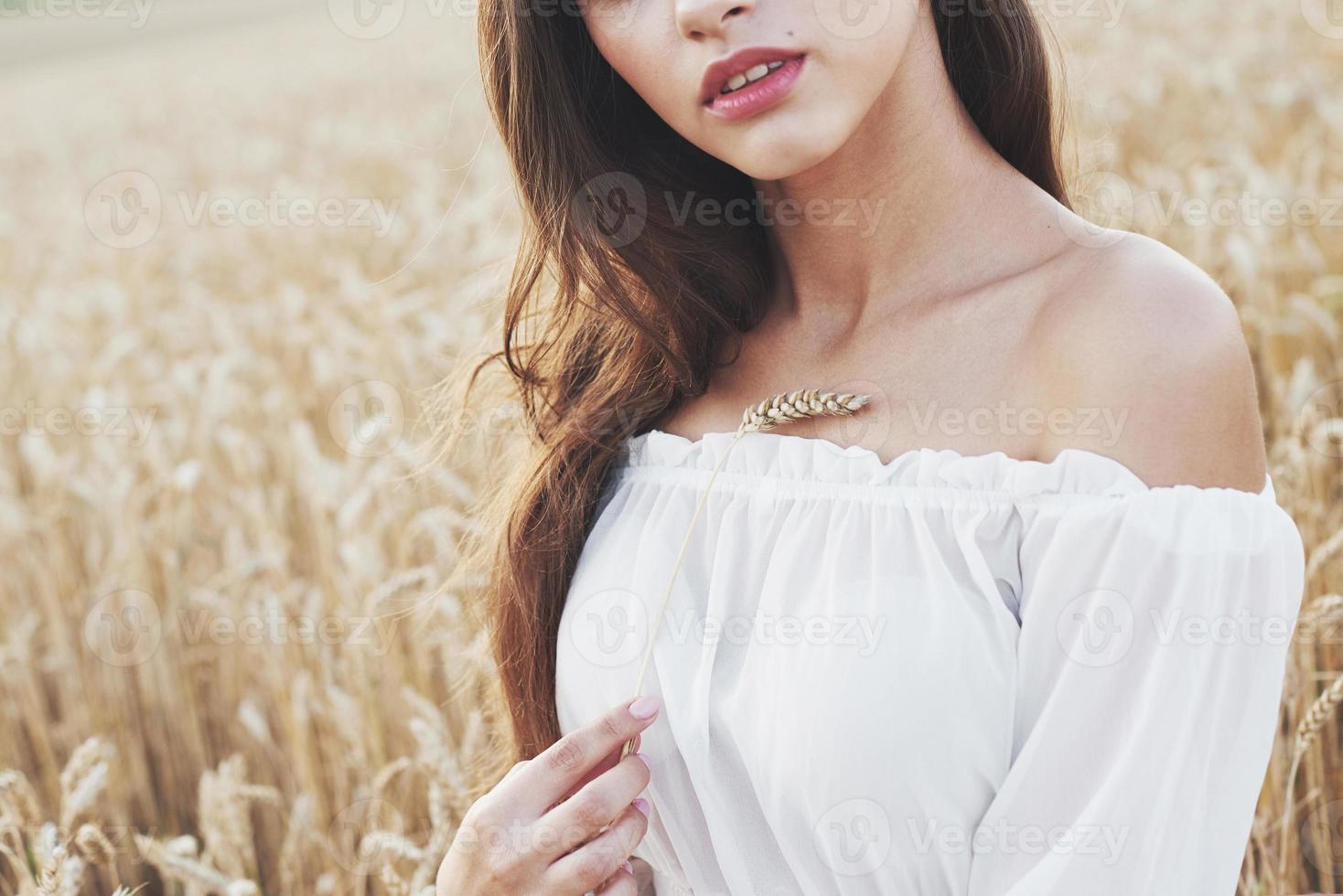 Sensible joven vestida de blanco posando en un campo de trigo dorado foto