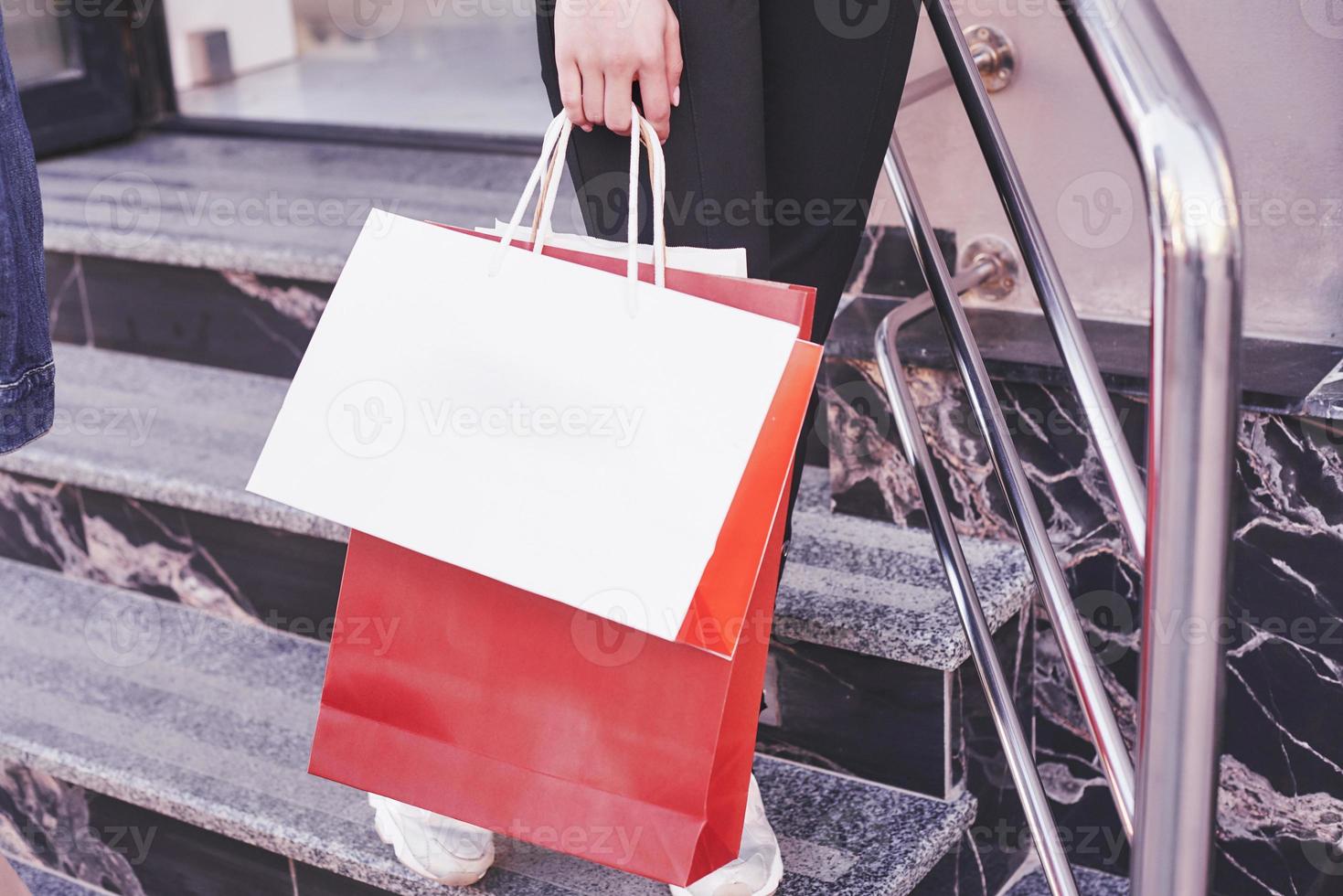 Cerrar joven llevando bolsas de la compra mientras camina por las escaleras después de visitar las tiendas foto
