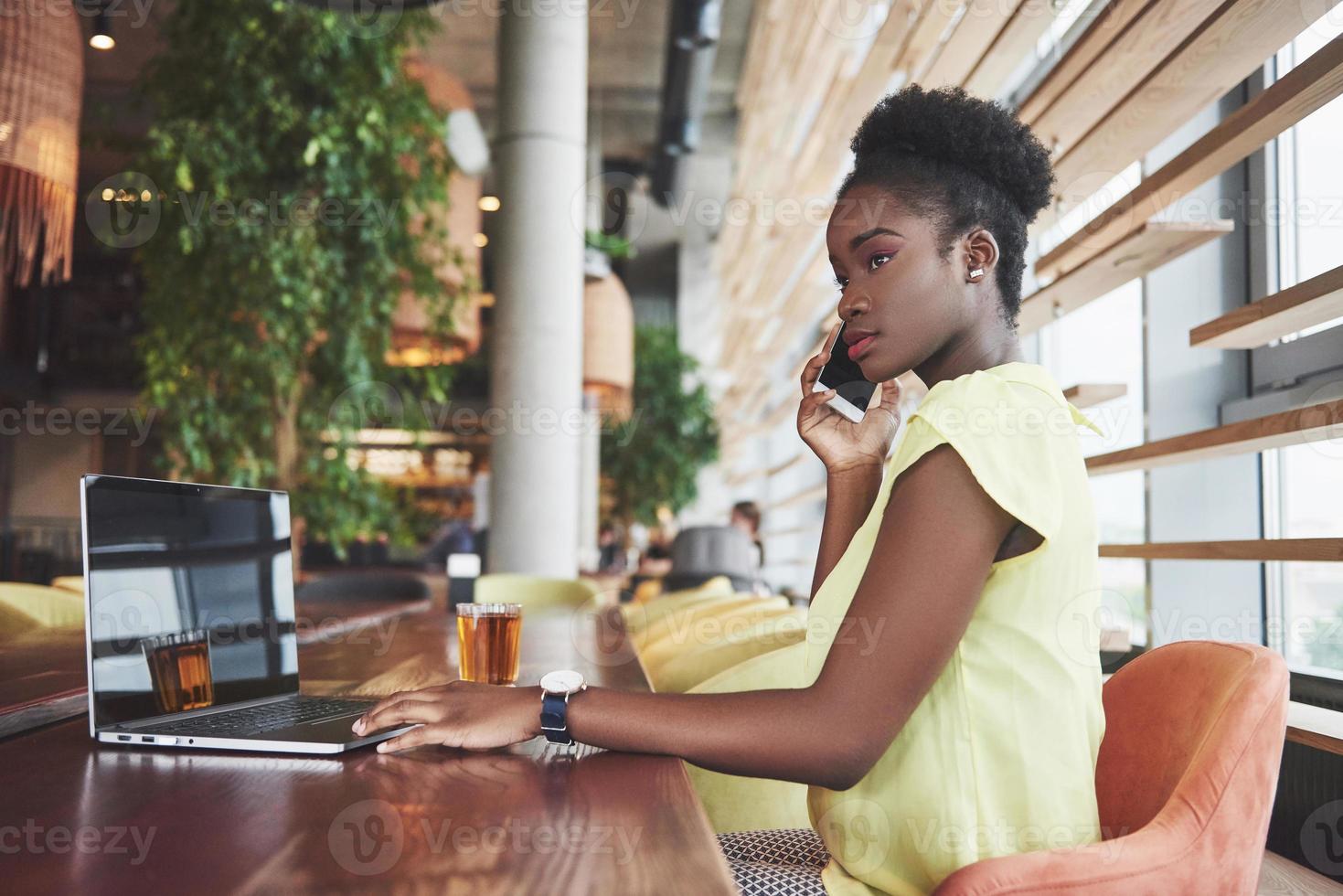 Joven y bella mujer de negocios afroamericana hablando por teléfono mientras trabajaba en un café foto