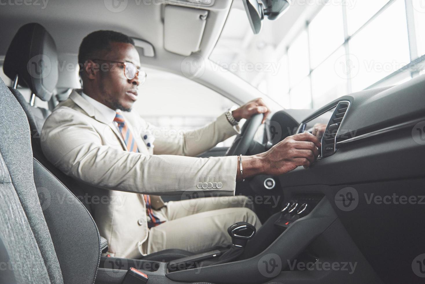 elegante hombre de negocios negro sentado al volante del nuevo coche de lujo. rico hombre afroamericano foto