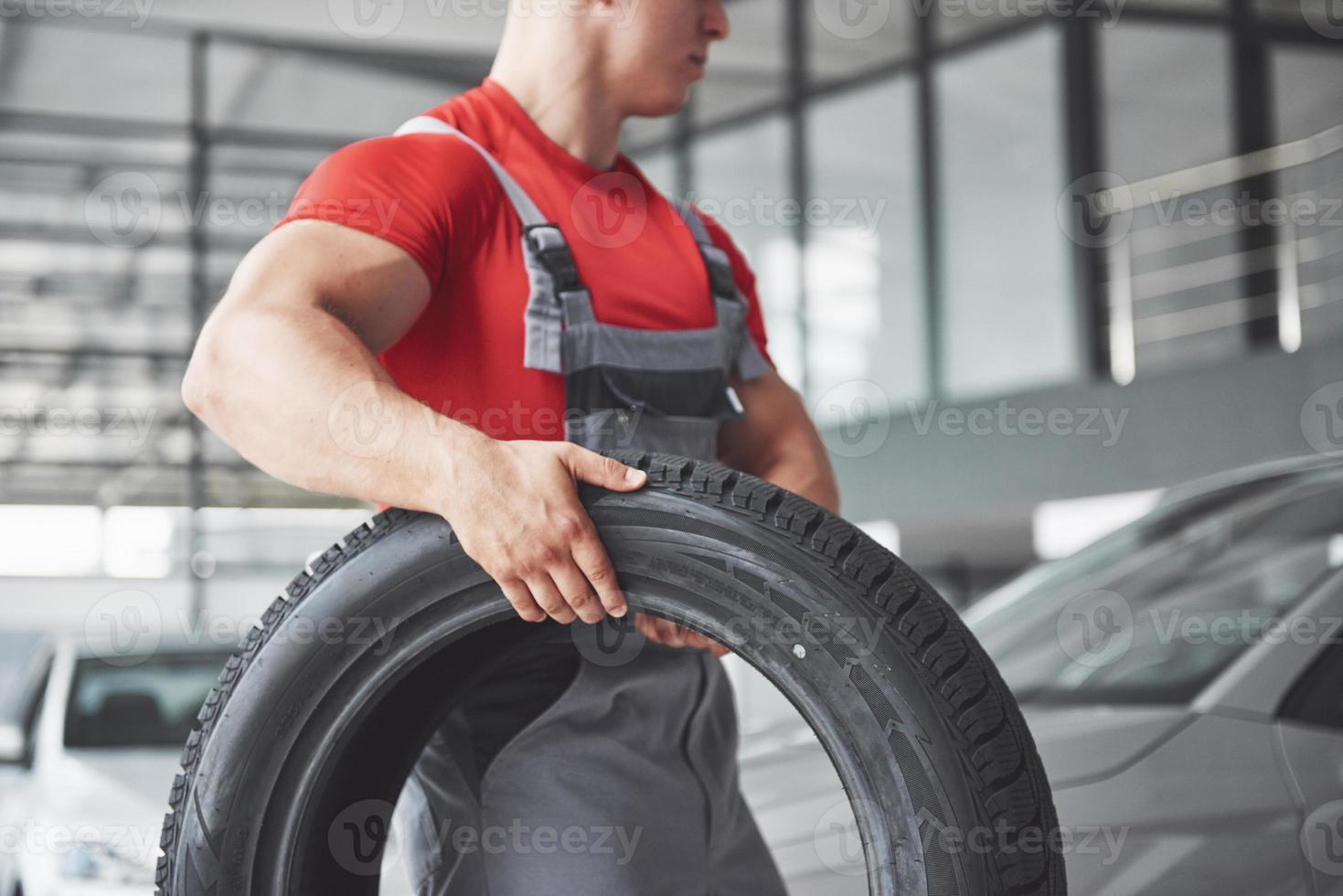 mecánico sosteniendo un neumático en el taller de reparación. sustitución de neumáticos de invierno y verano. foto