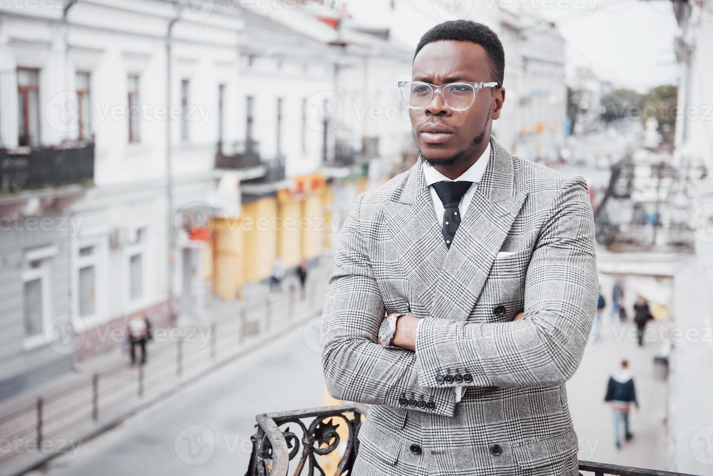Confident black business man in a stylish suit standing on office block looking at the camera with a serious expression photo