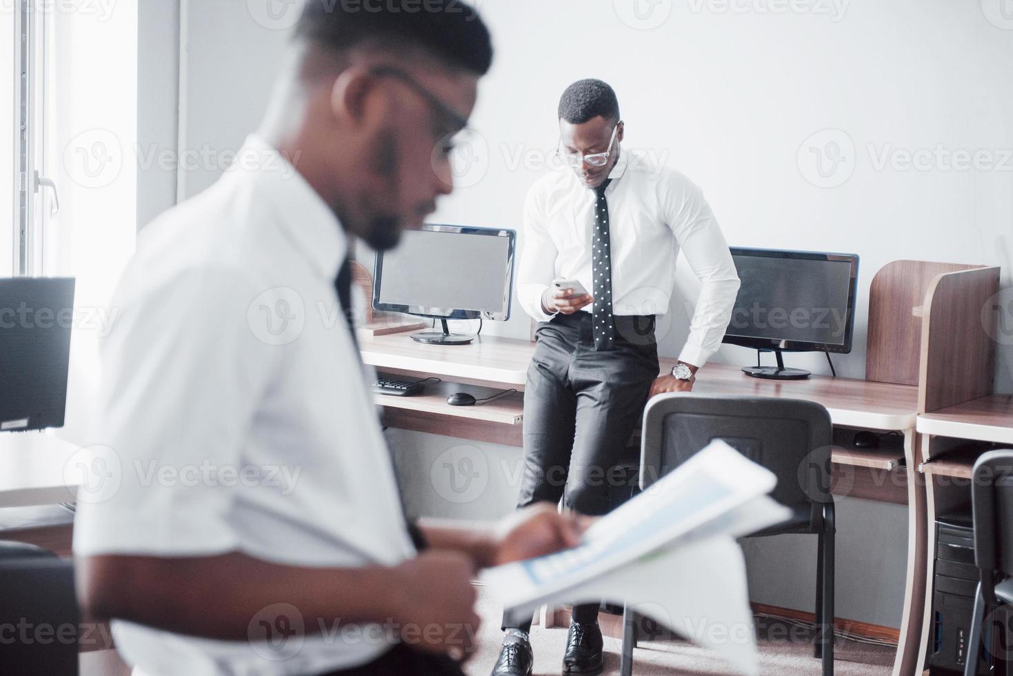 discutir un proyecto. Dos hombres de negocios negros en ropa formal discutiendo algo mientras uno de ellos apunta un papel foto