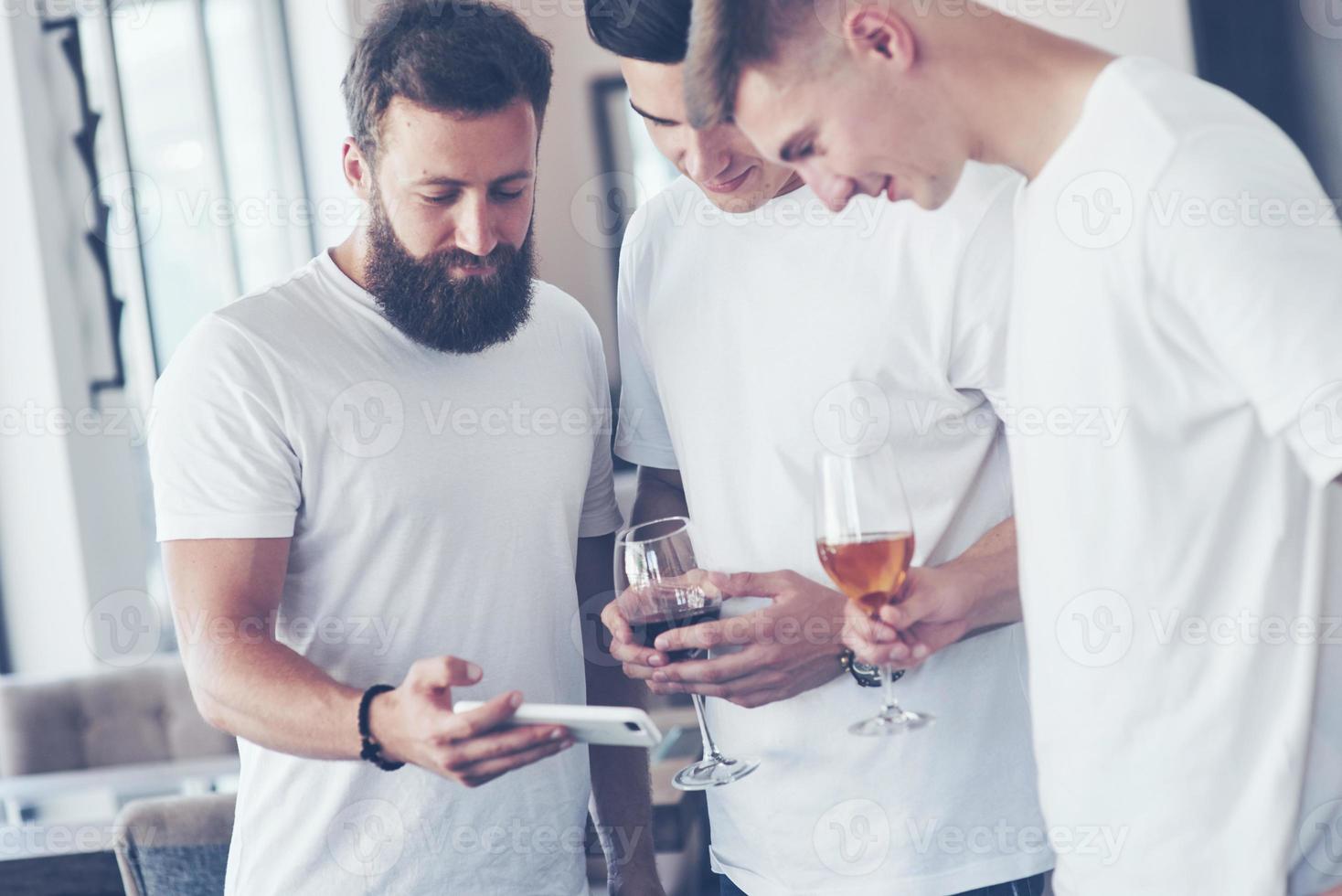 alegres viejos amigos se comunican entre sí y miran el teléfono, con vasos de whisky o vino en el pub. concepto de entretenimiento y estilo de vida. gente conectada wifi en reunión de mesa de bar foto