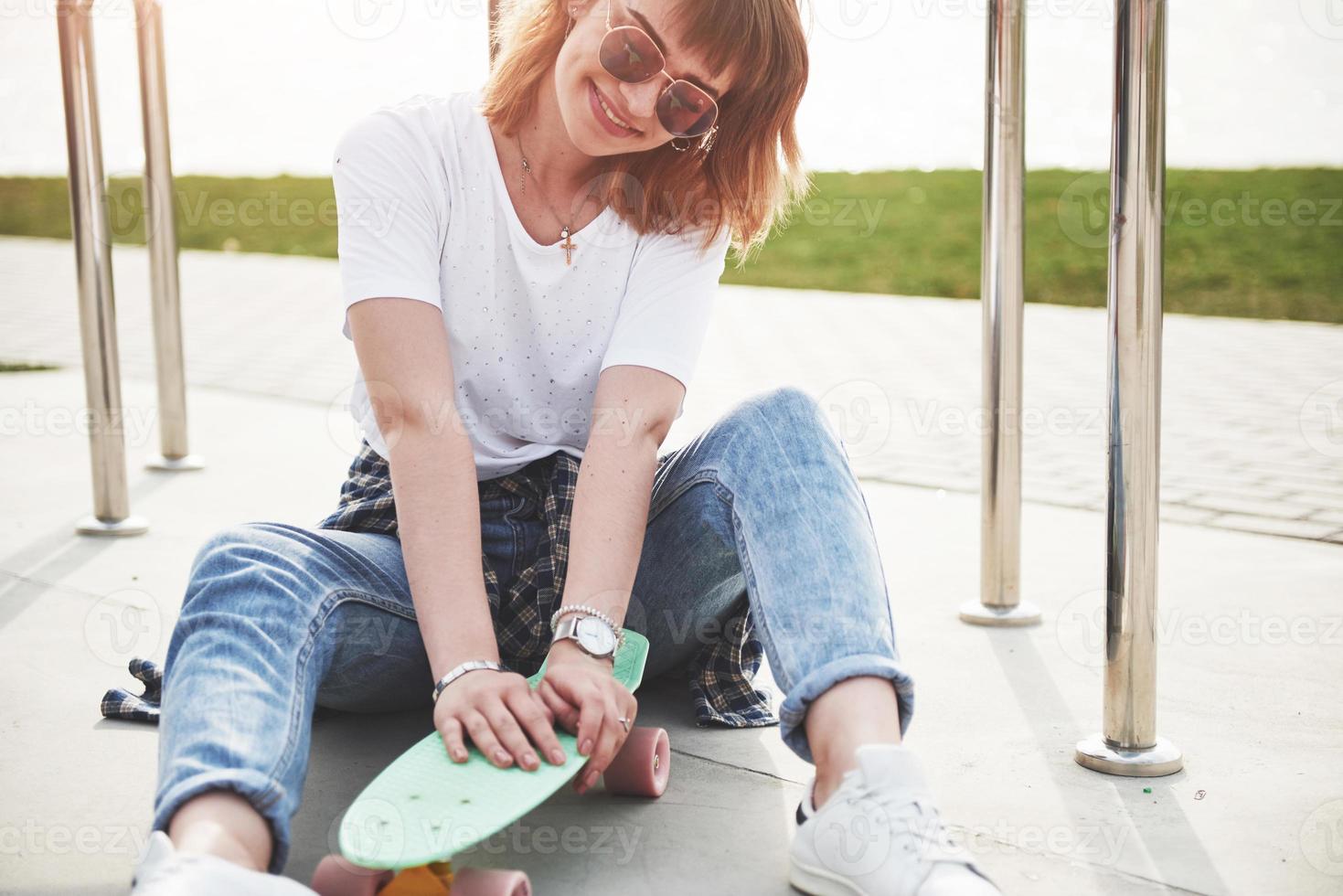 Una hermosa joven se divierte en el parque y monta una patineta. foto