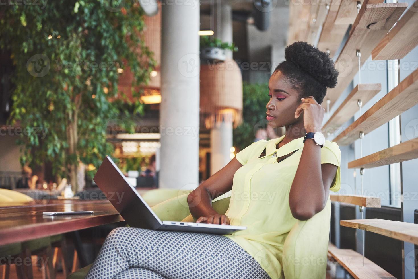 Hermosa mujer joven sentada en un café y trabajando en una computadora portátil foto