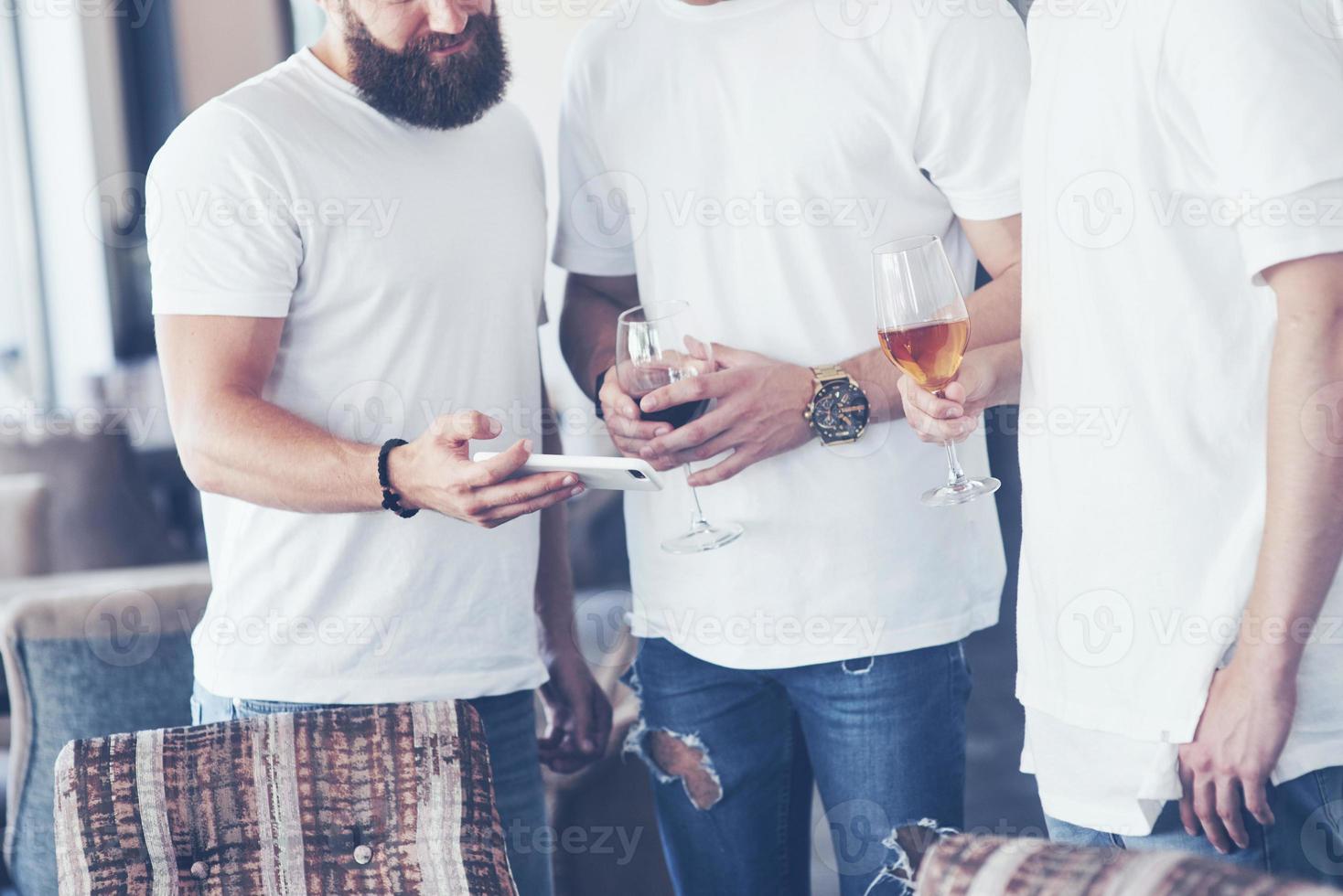 Cheerful old friends communicate with each other and phone watch, with glasses of whiskey or wine in pub. Concept of entertainment and lifestyle. Wifi connected people in bar table meeting photo