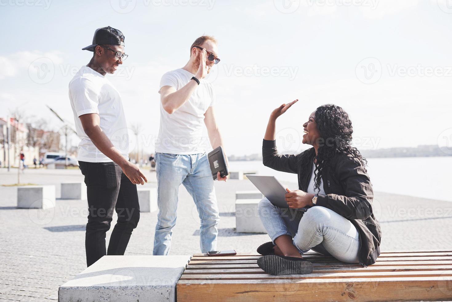 hermosos amigos multiétnicos usando una computadora portátil en la calle. concepto de estilo de vida juvenil foto