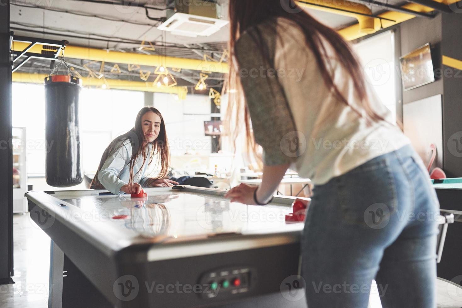 dos hermosas niñas gemelas juegan air hockey en la sala de juegos y se divierten foto