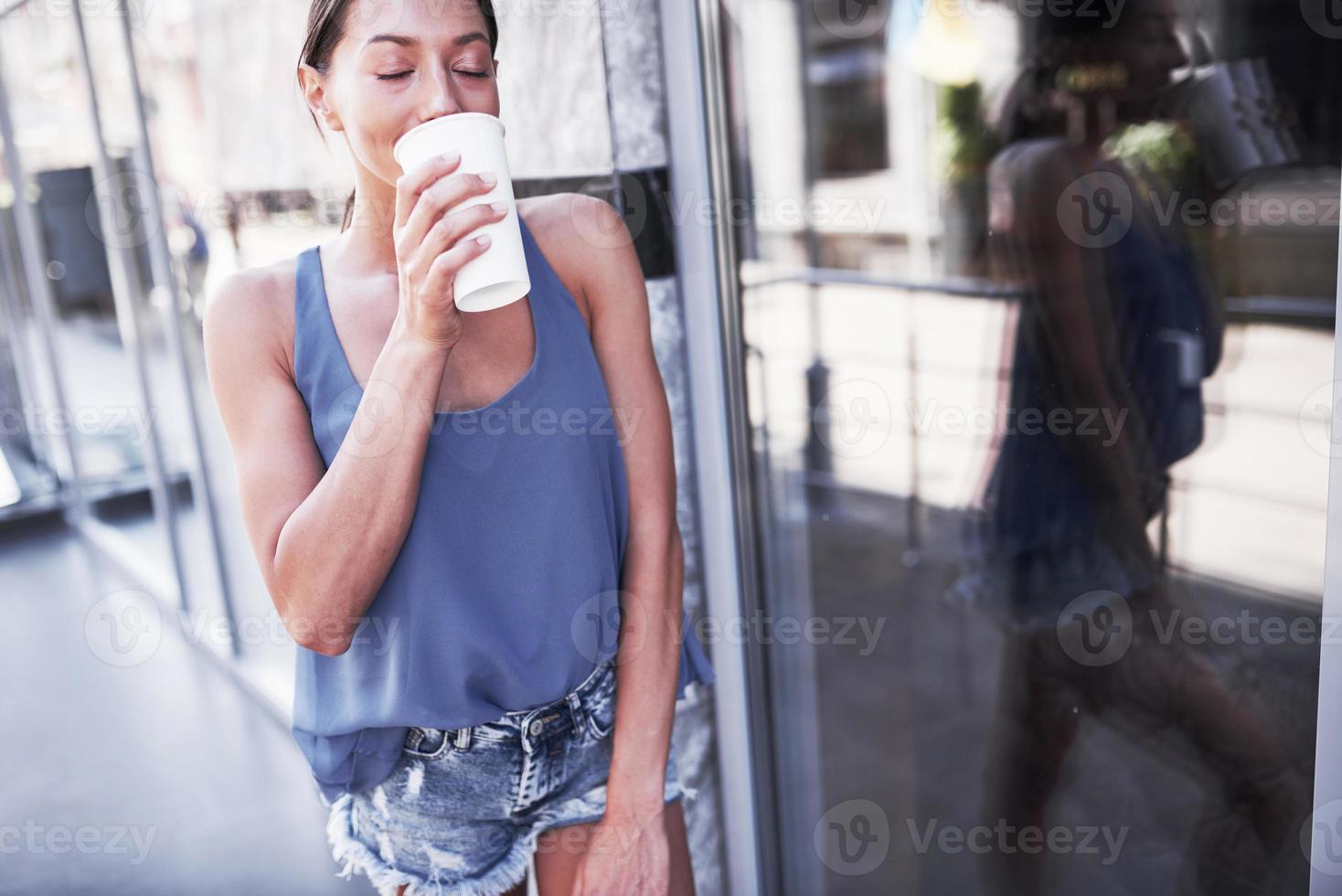 Retrato de mujer joven inconformista con estilo caminando en la calle, vistiendo un lindo atuendo de moda, bebiendo café con leche caliente y sonriendo foto