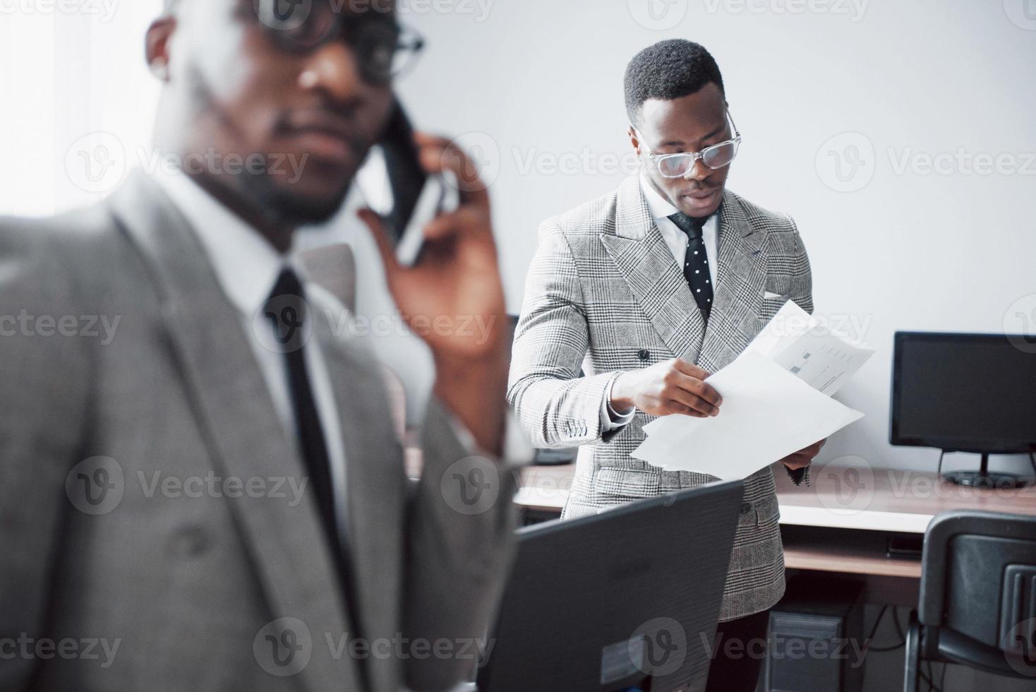 Modern businessman at work. Two confident business people in formalwear discussing something While one of them looks at the documents and the second an important phone call photo