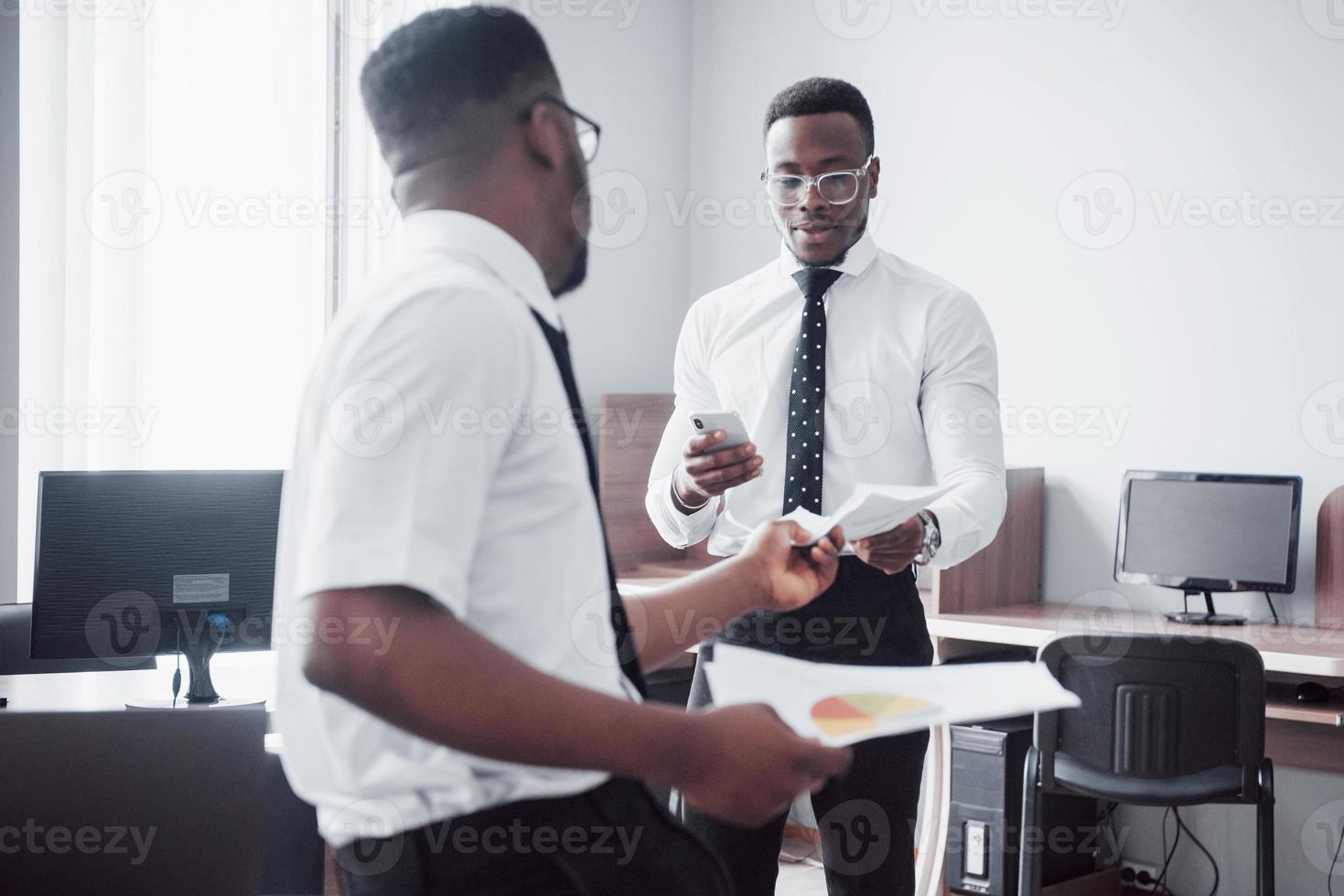 discutir un proyecto. Dos hombres de negocios negros en ropa formal discutiendo algo mientras uno de ellos apunta un papel foto