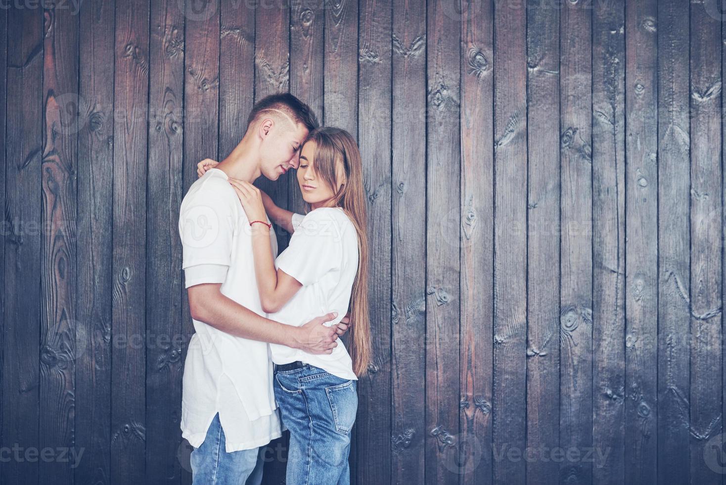 Young couple, guy and girl together on a wooden wall background. They are happy together and dressed alike. Always in a trend photo