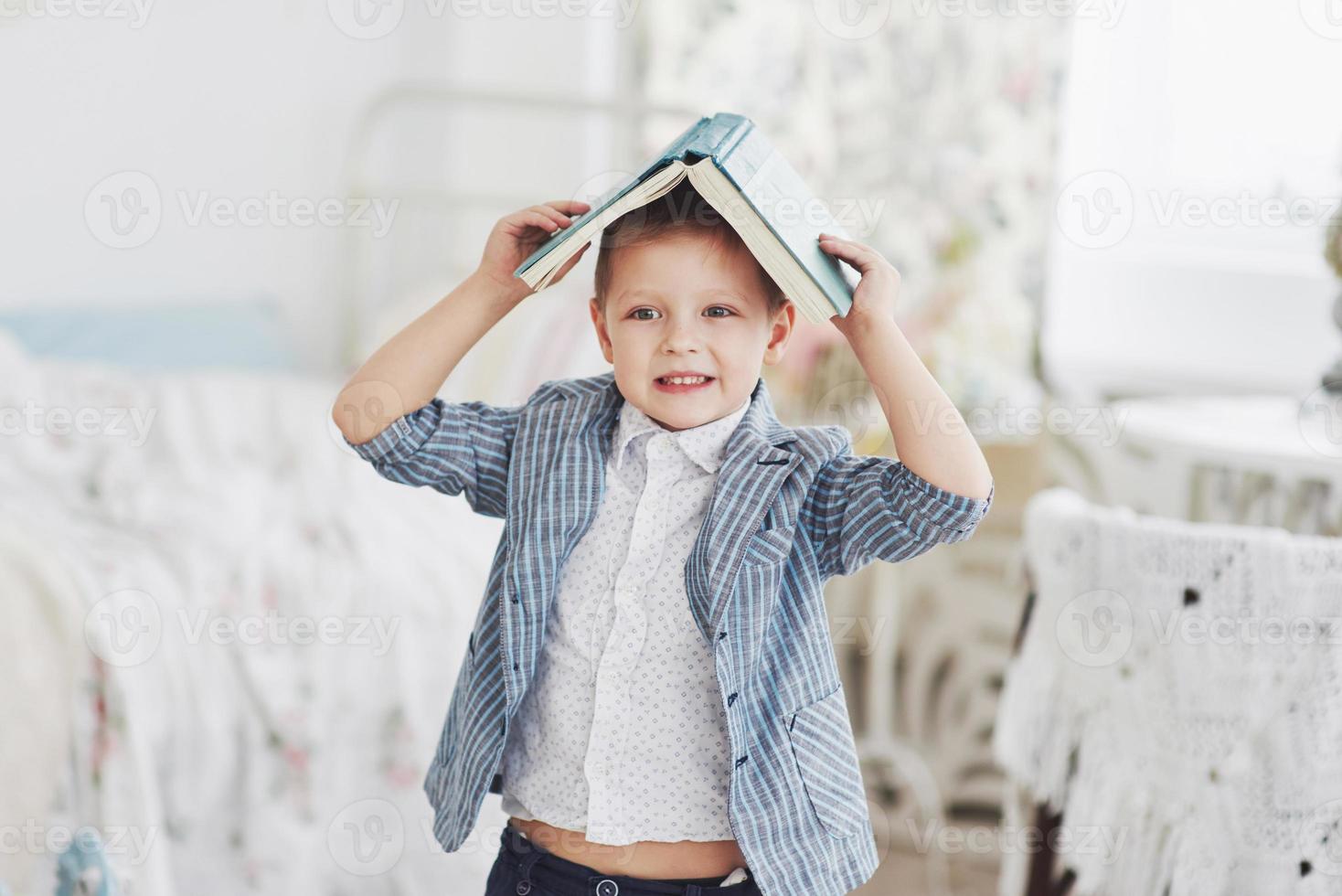 Photo of diligent schoolboy with book on his head doing homework. The schoolboy is tired of doing homework