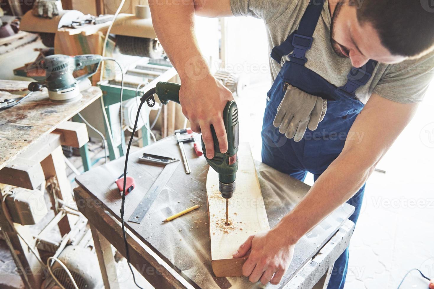 The master works in a studio and drill a hole in a wooden board. photo