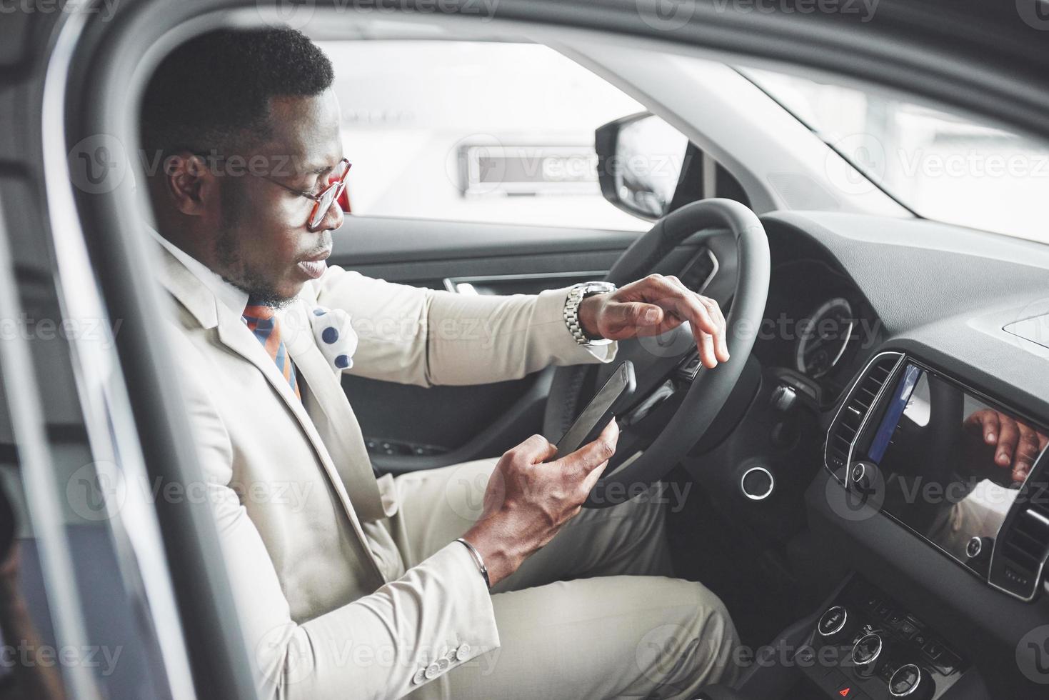 elegante hombre de negocios negro sentado al volante del nuevo coche de lujo. rico hombre afroamericano foto