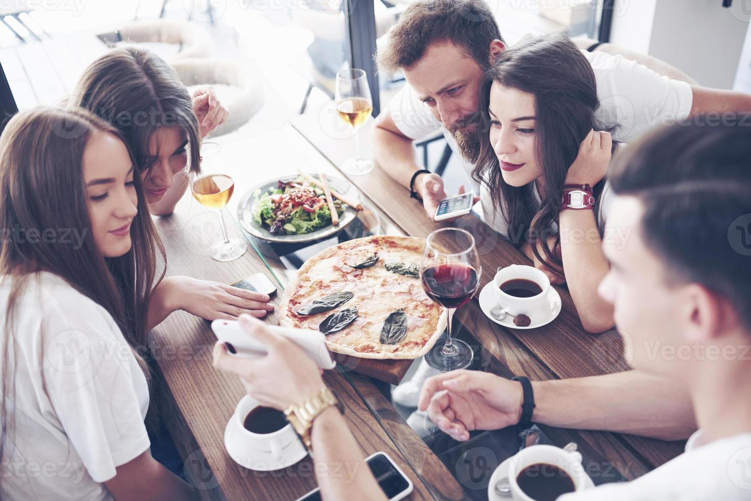 Sabrosa pizza en la mesa, con un grupo de jóvenes sonrientes descansando en el pub foto