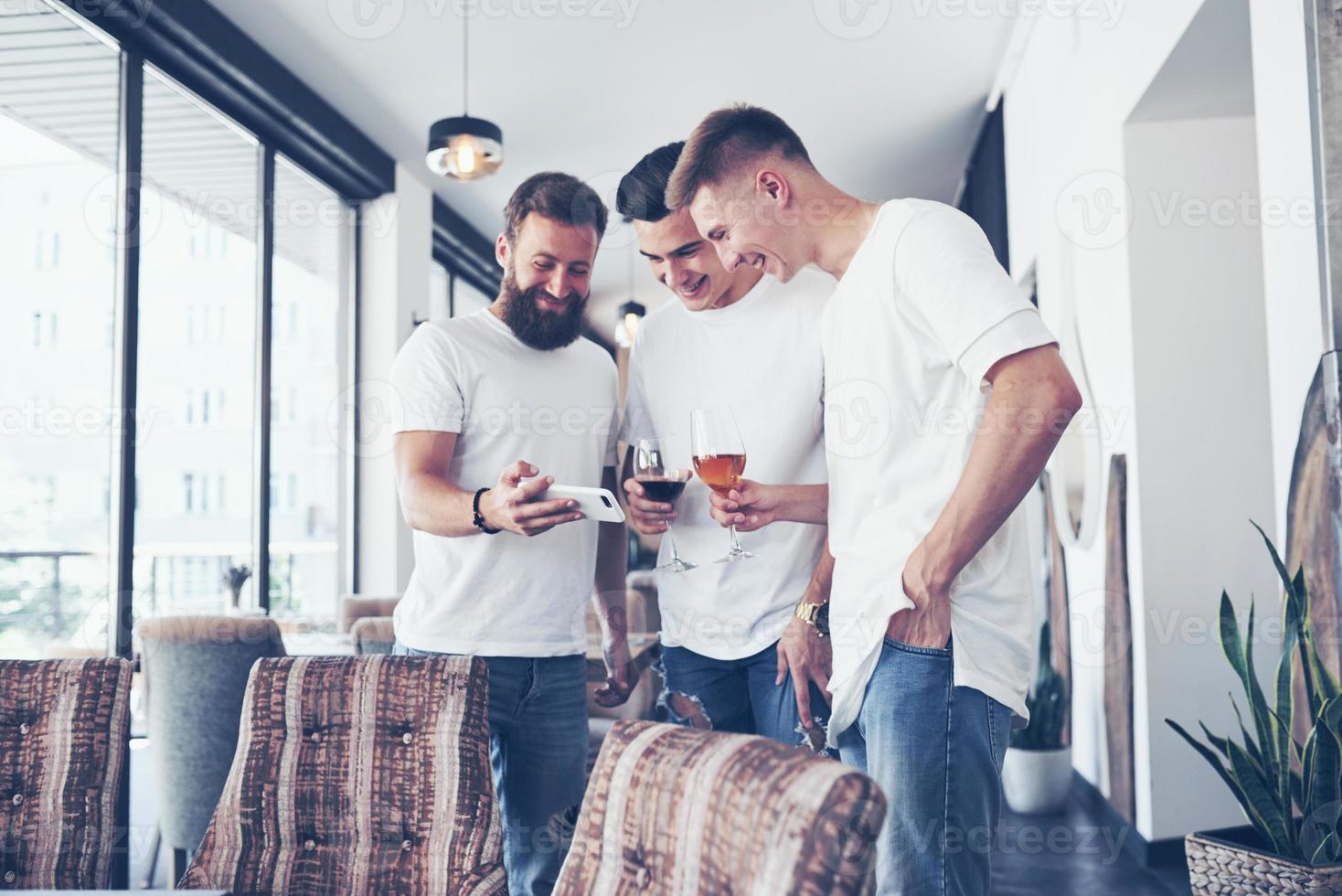 alegres viejos amigos se comunican entre sí y miran el teléfono, con vasos de whisky o vino en el pub. concepto de entretenimiento y estilo de vida. gente conectada wifi en reunión de mesa de bar foto