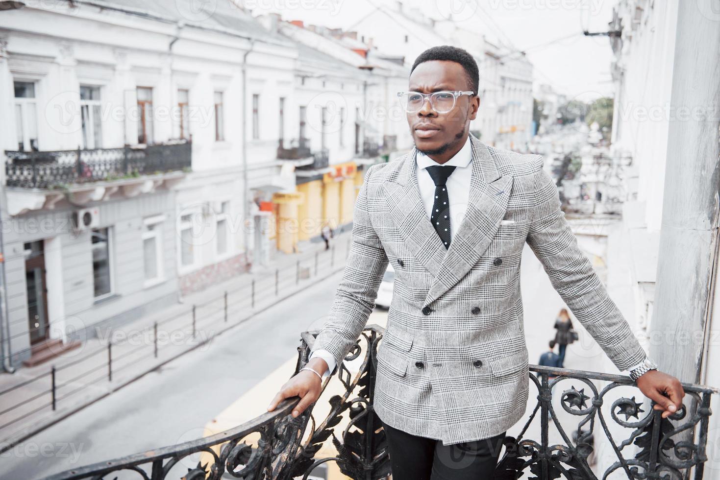 Hombre de negocios negro confiado en un elegante traje de pie en el bloque de oficinas mirando a la cámara con una expresión seria foto