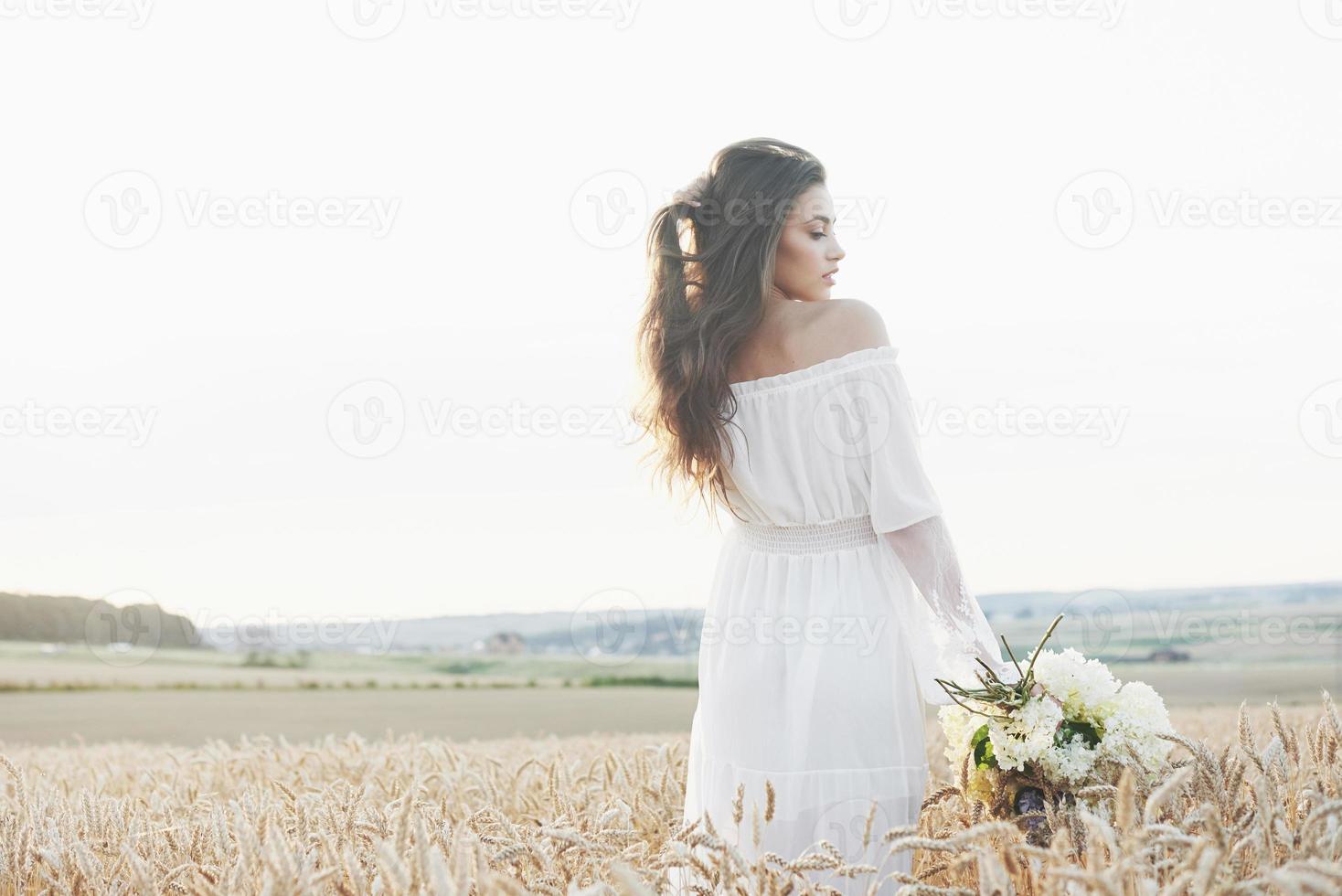 Beautiful girl in white dress running on the autumn field of wheat at sunset time photo