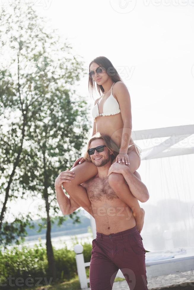 Happy young man wearing his wife on the shoulders of the beach photo