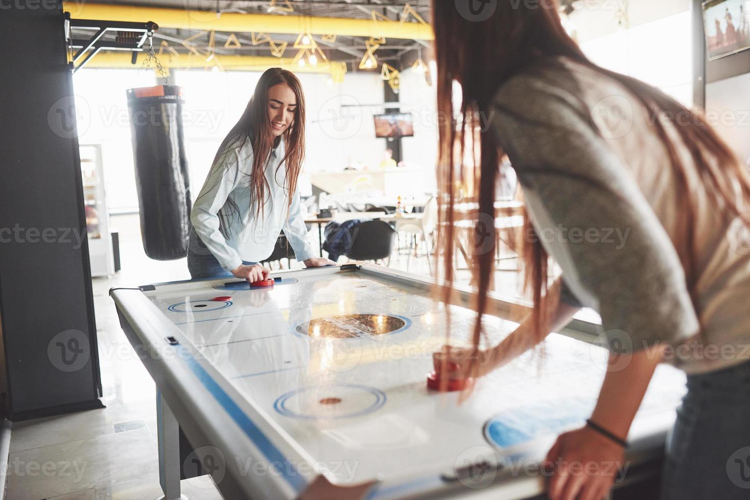 Two beautiful twin girls play air hockey in the game roomand have fun photo