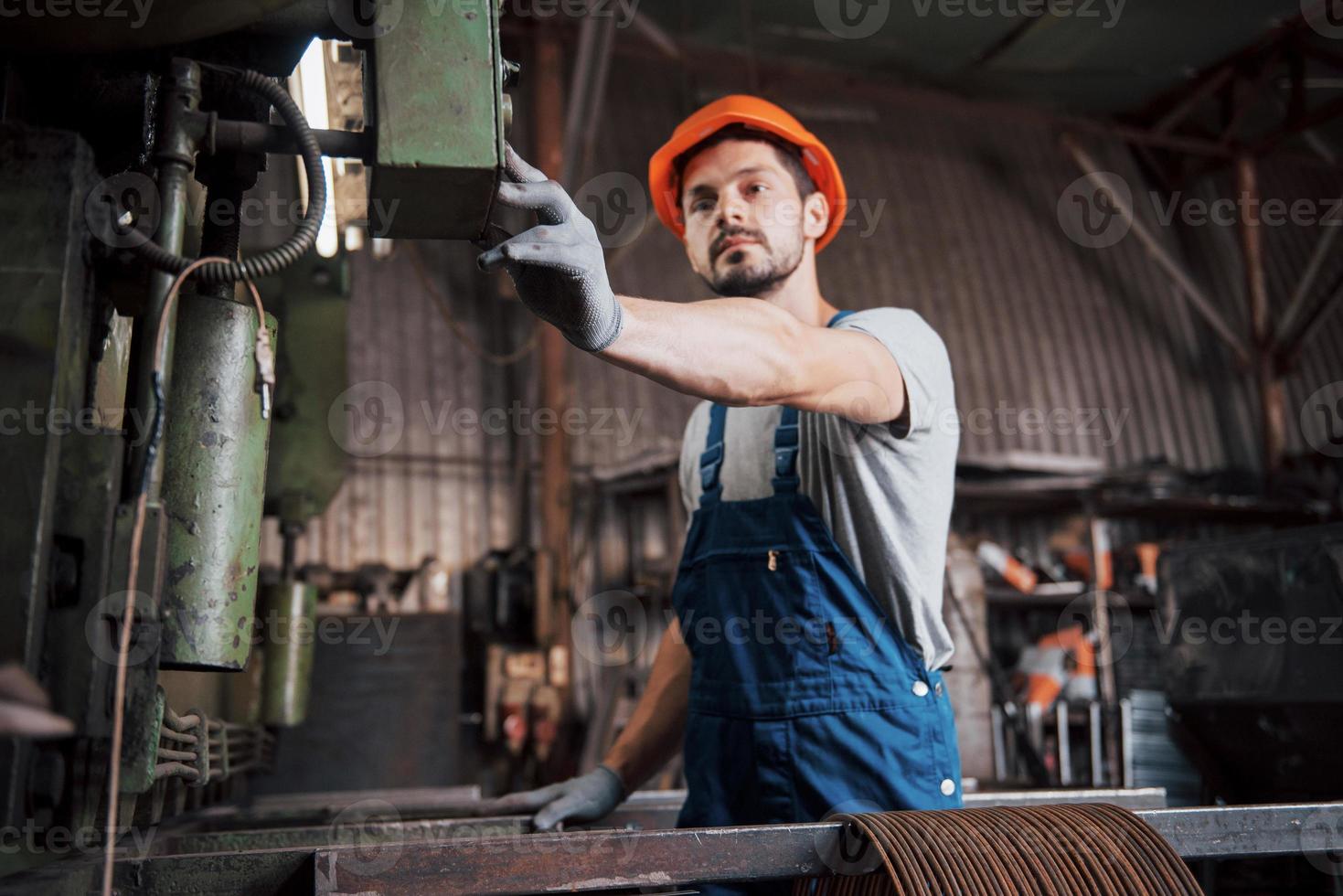retrato de un joven trabajador con casco en una gran fábrica de reciclaje de residuos. el ingeniero supervisa el trabajo de las máquinas y otros equipos foto