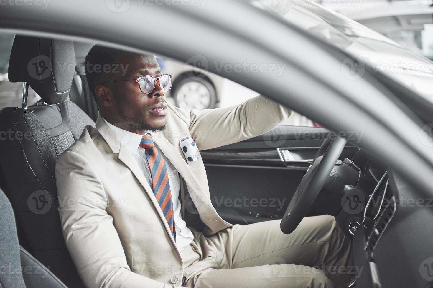 elegante hombre de negocios negro sentado al volante del nuevo coche de lujo. rico hombre afroamericano foto