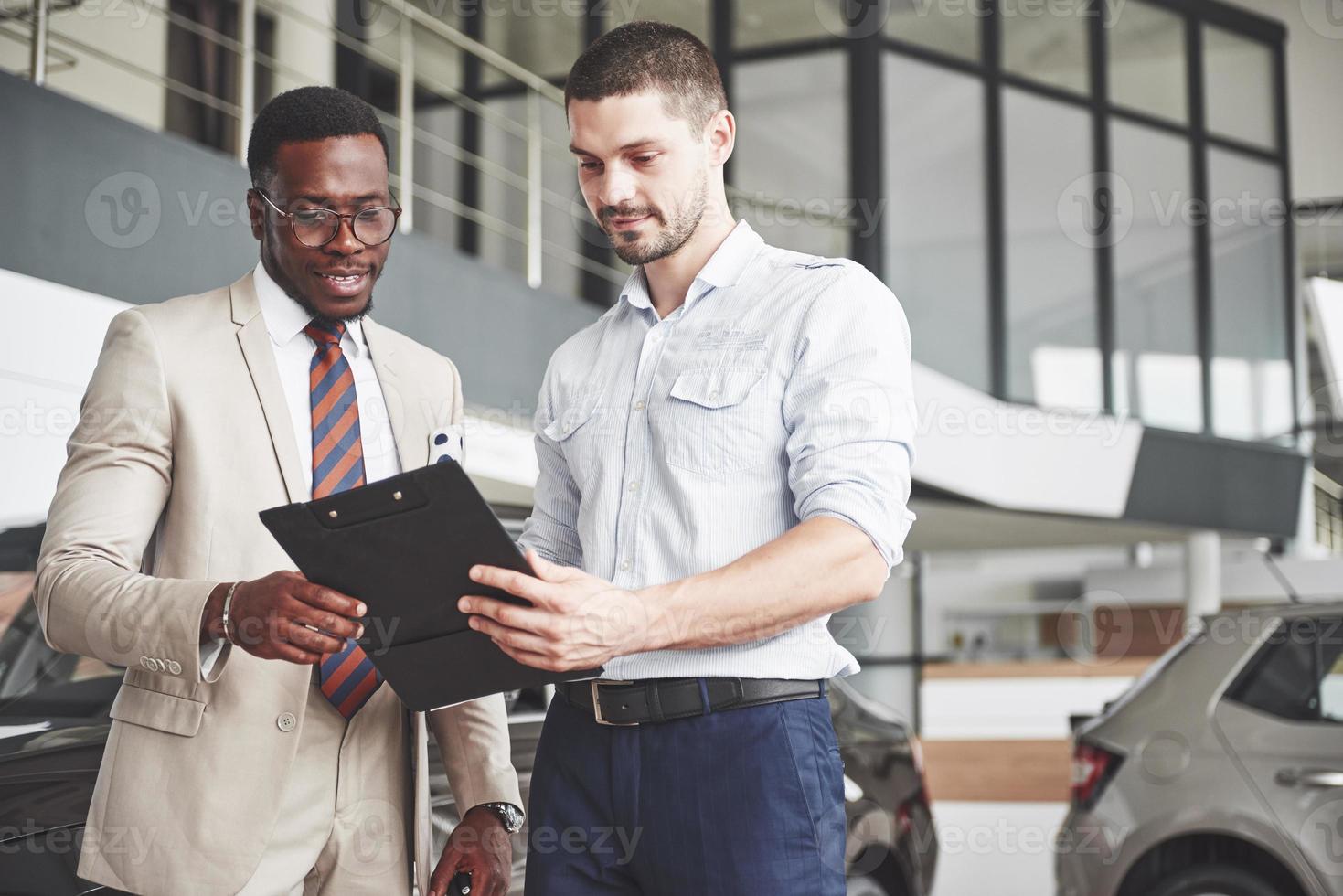 A young black businesswoman signs documents and buys a new car. The car dealer is standing next to him photo