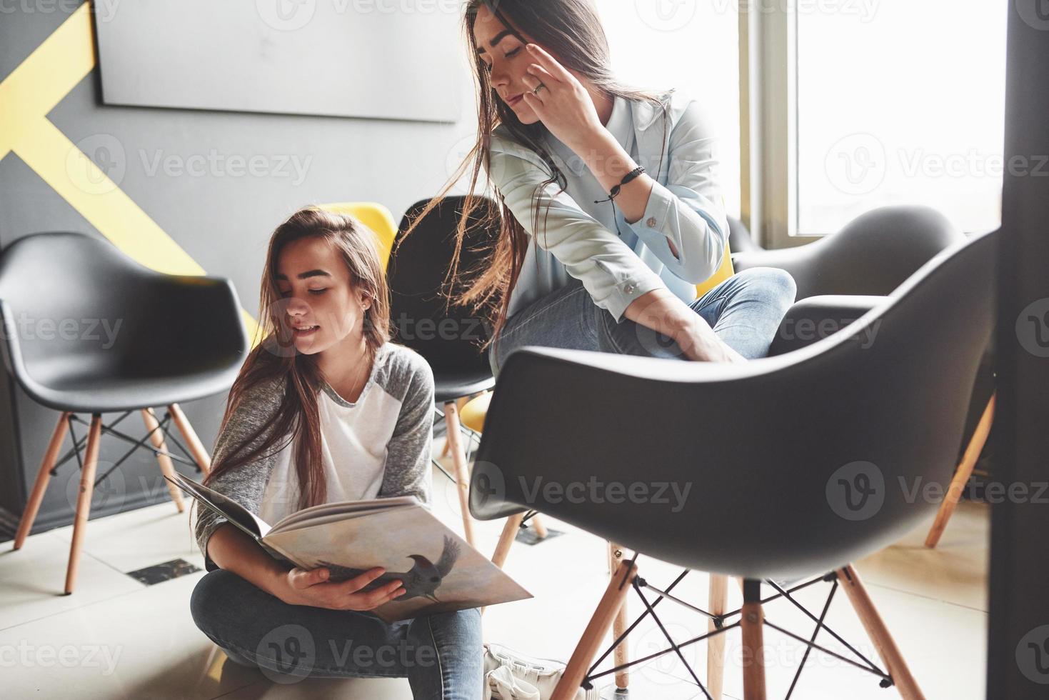 Two beautiful twin girls spend time read a book in library in the morning. Sisters relaxing in a cafe and having fun together photo
