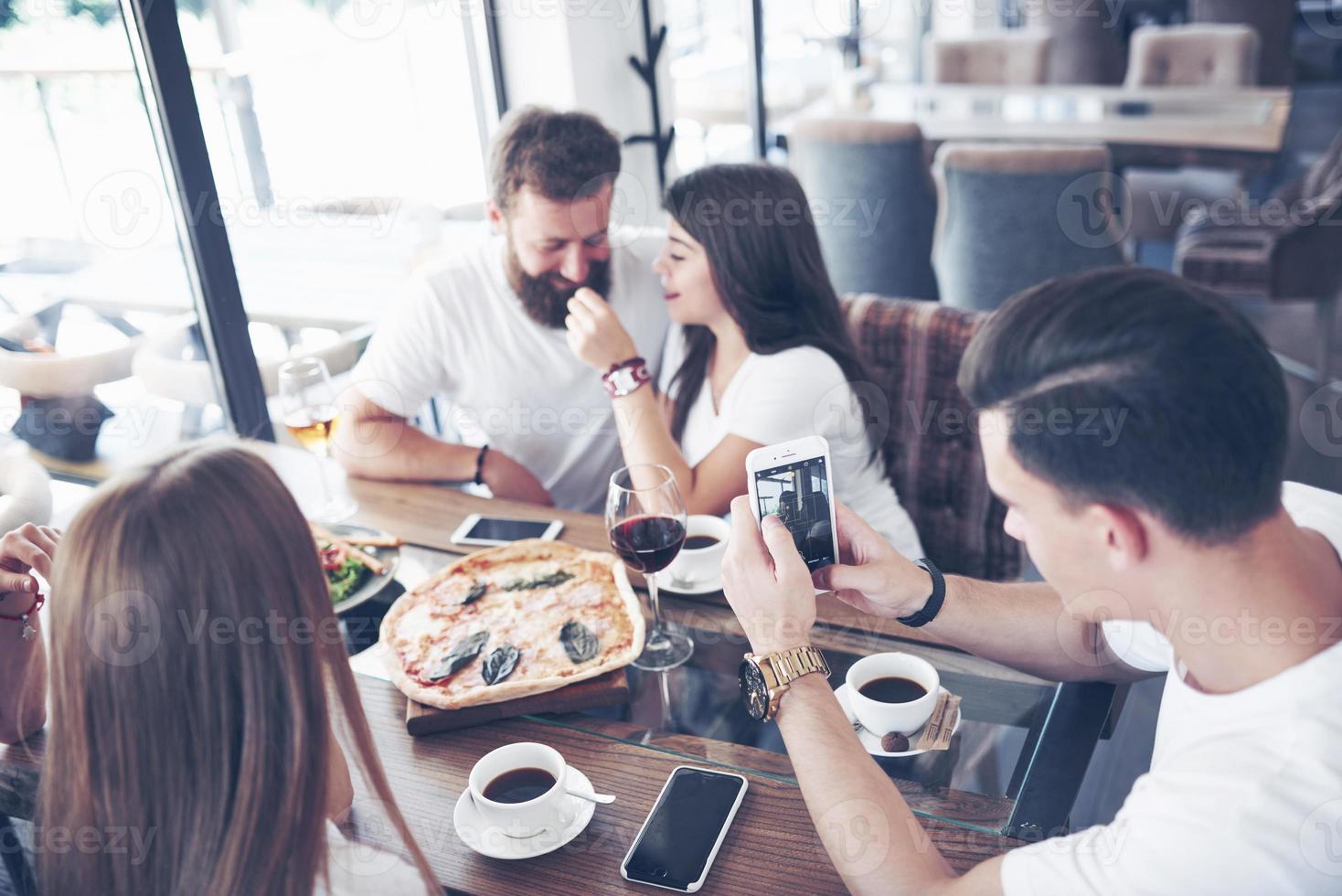 Sabrosa pizza en la mesa, con un grupo de jóvenes sonrientes descansando en el pub foto