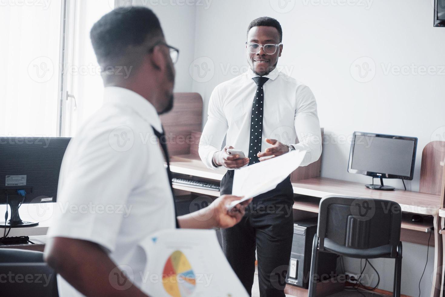 discutir un proyecto. Dos hombres de negocios negros en ropa formal discutiendo algo mientras uno de ellos apunta un papel foto