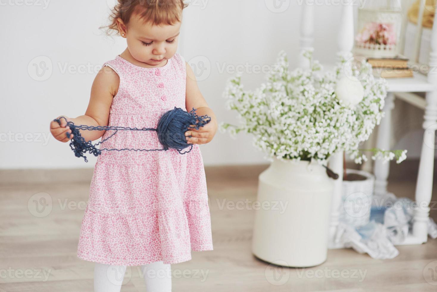 concepto de infancia. niña con vestido lindo jugar con hilo de colores. habitación infantil blanca vintage foto