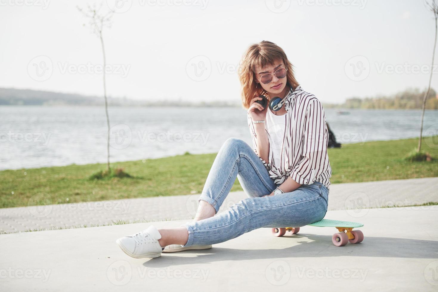 Una hermosa joven se divierte en el parque y monta una patineta. foto