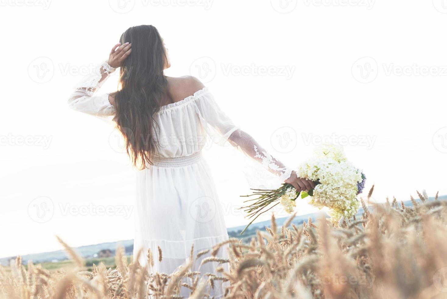 Sensible joven vestida de blanco posando en un campo de trigo dorado foto