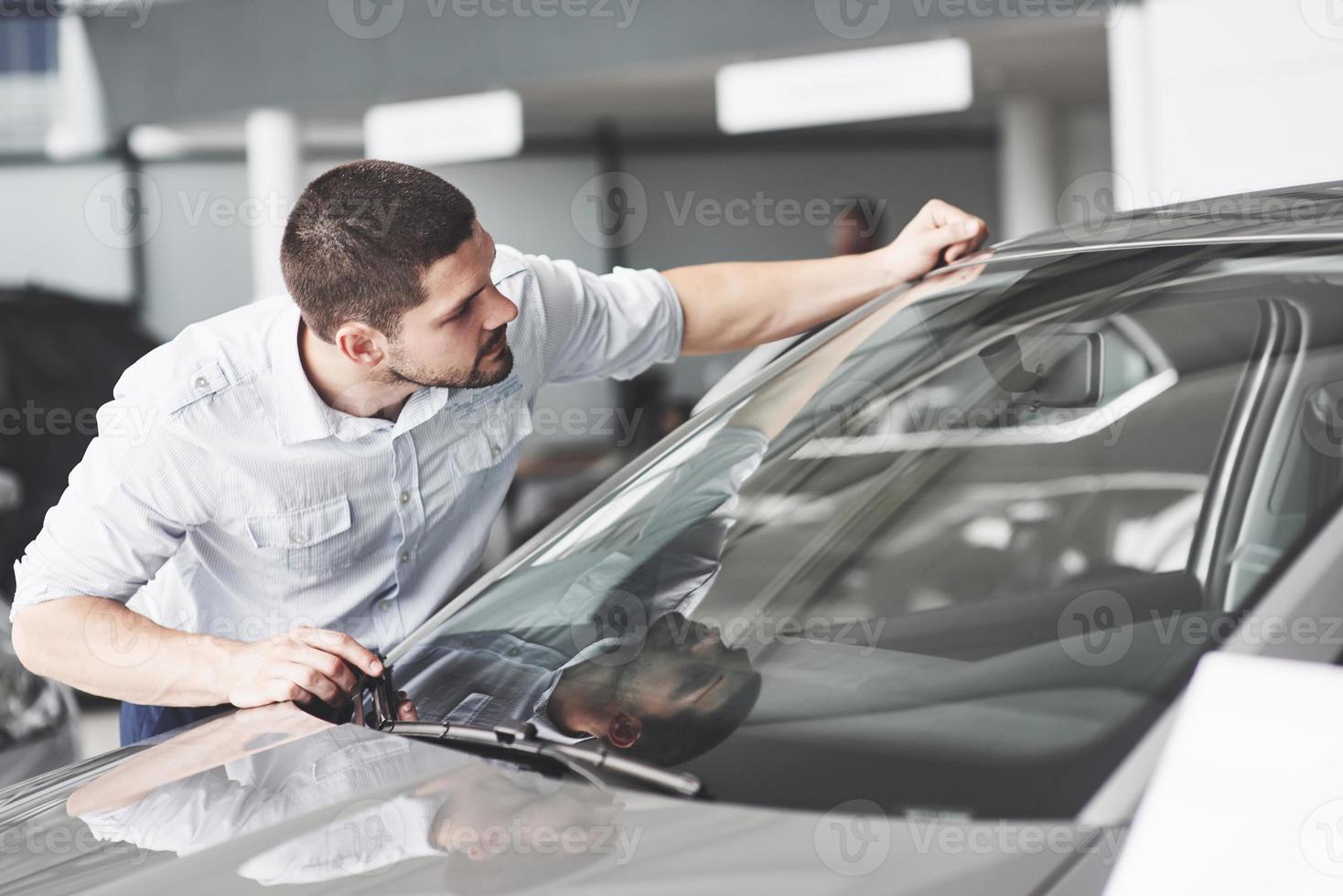 hombre feliz tocando el coche en el salón del automóvil o salón. foto