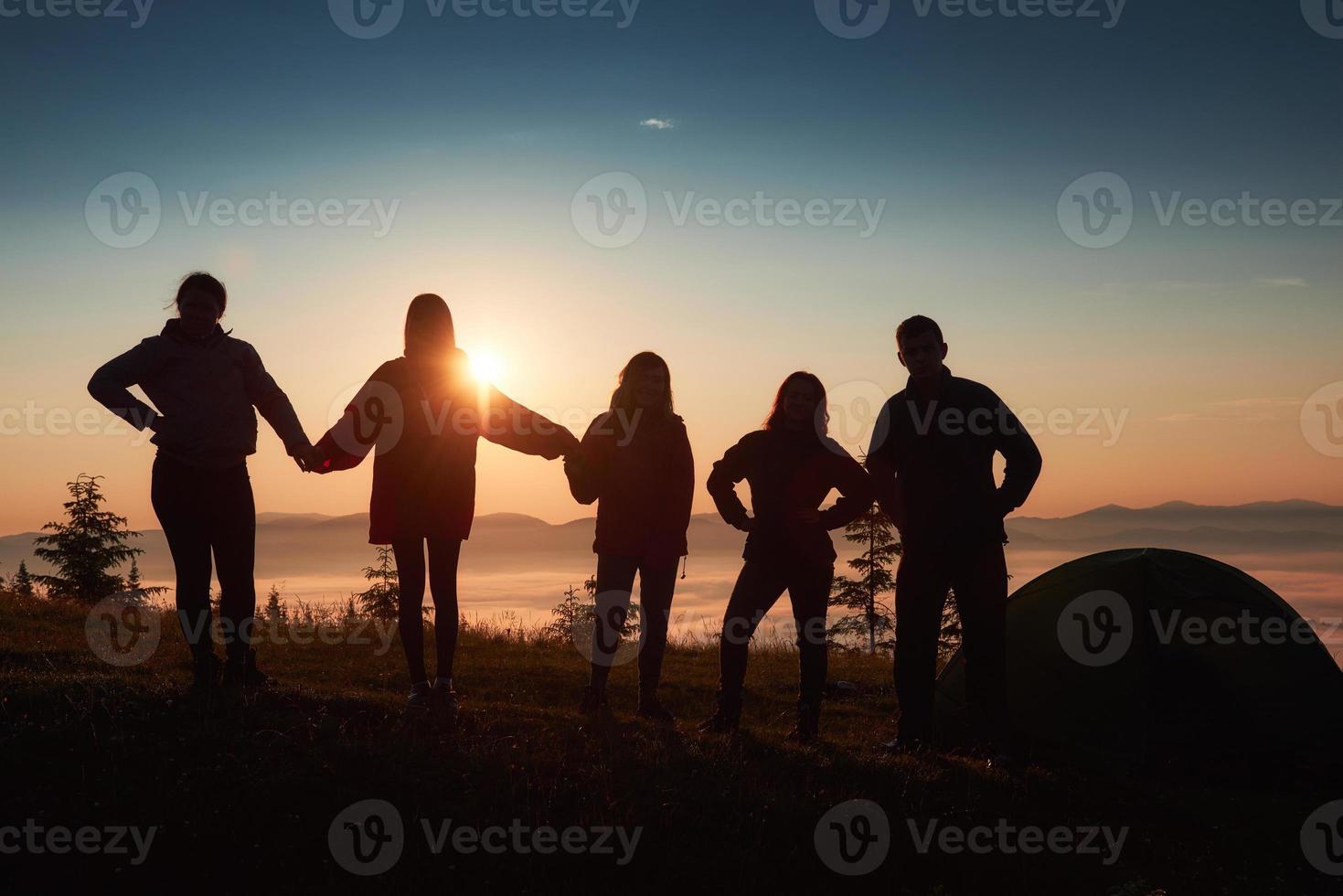 Una silueta de un grupo de personas se divierte en la cima de la montaña cerca de la carpa durante la puesta de sol. foto