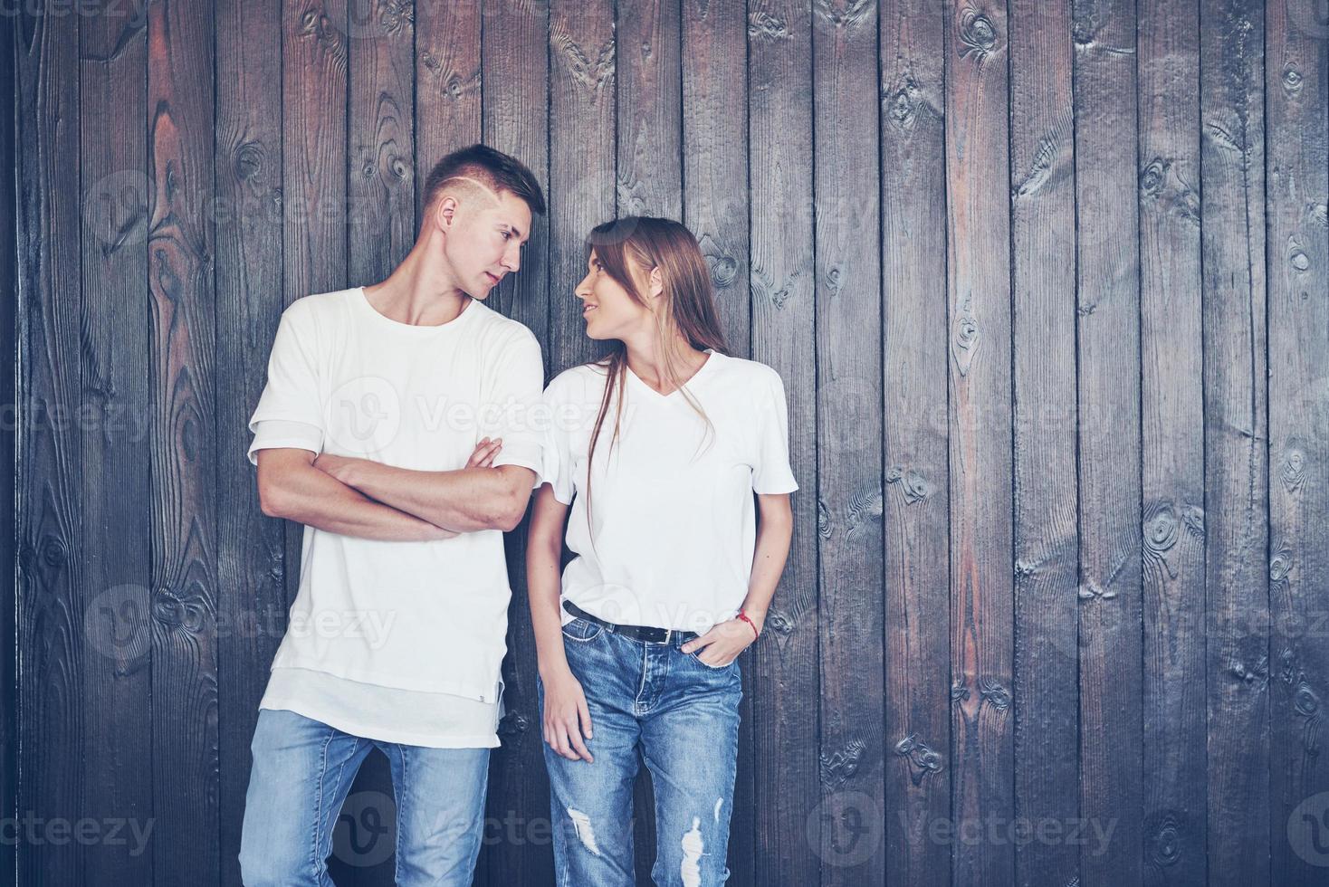 Young couple, guy and girl together on a wooden wall background. They are happy together and dressed alike. Always in a trend photo