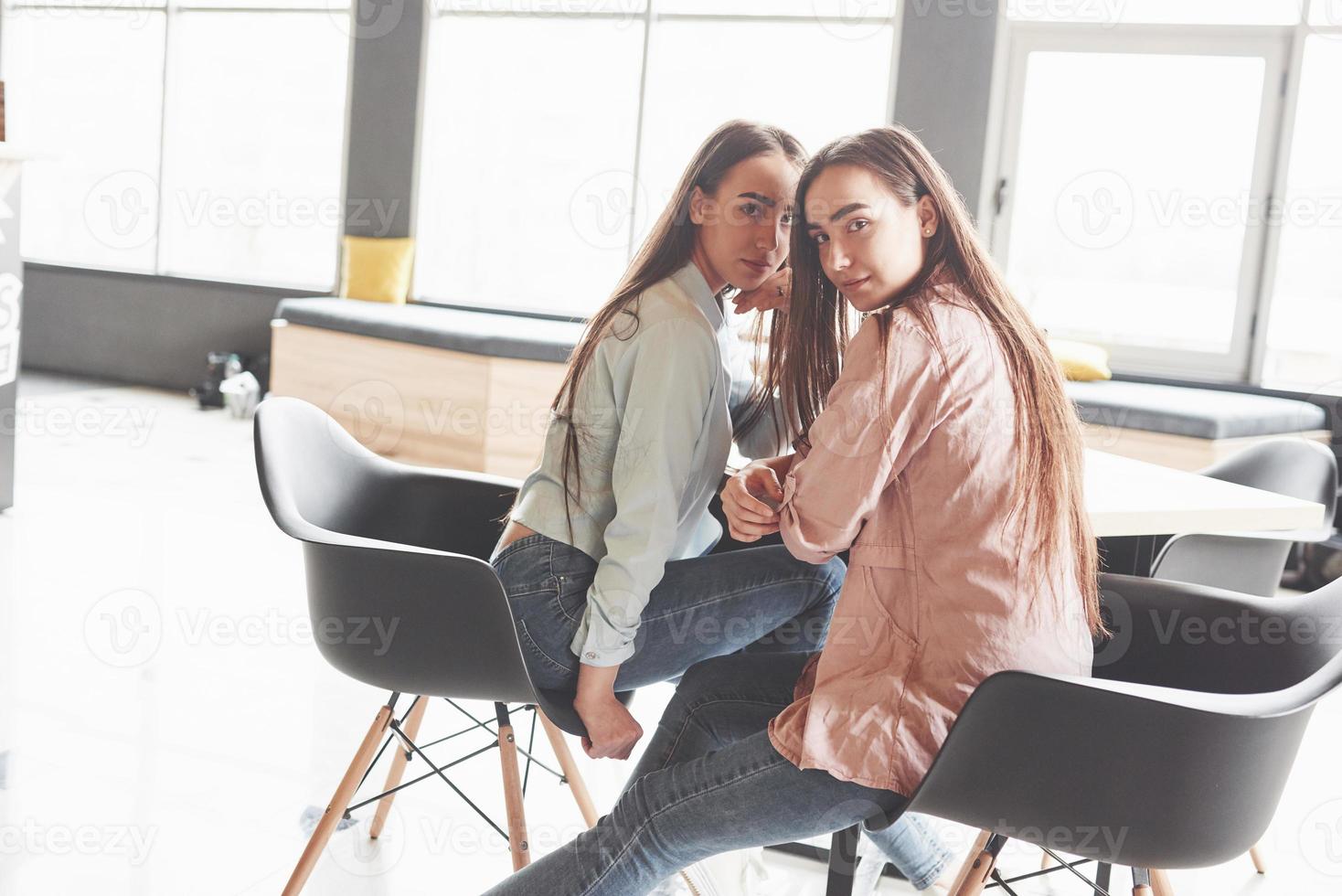 Two beautiful twin girls spend time. Sisters relaxing in a cafe and having fun together and whispering photo