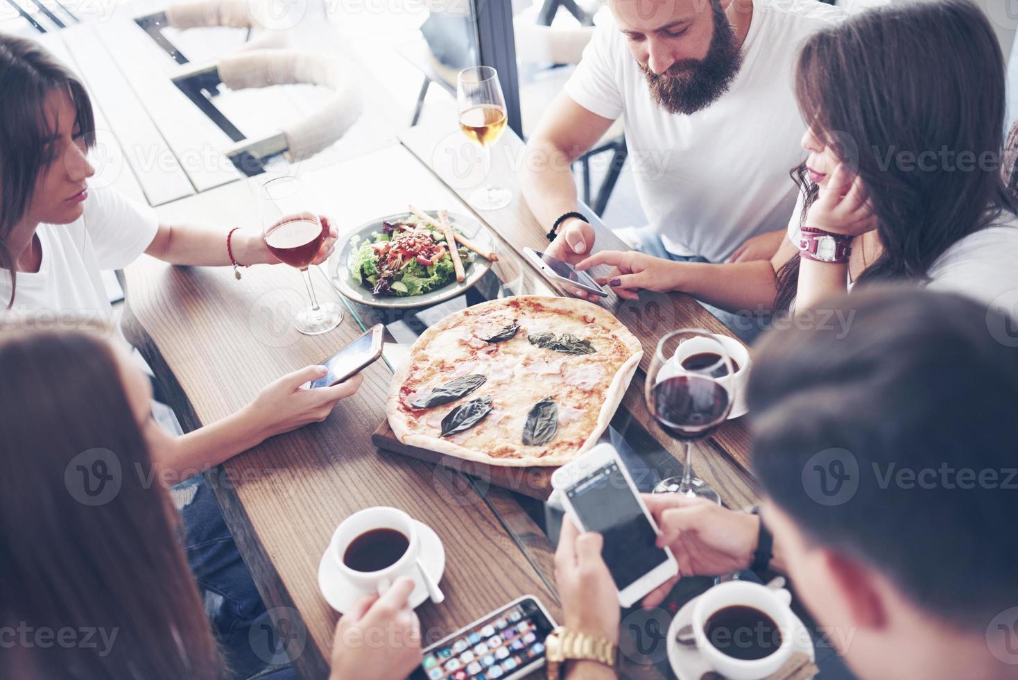 Sabrosa pizza en la mesa, con un grupo de jóvenes sonrientes descansando en el pub foto