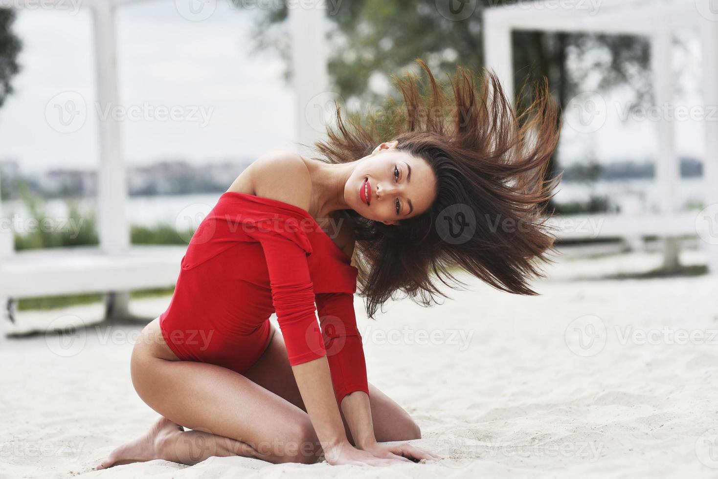 una chica sexy en traje de baño rojo posa para el fotógrafo. hermosa morena con cabello largo relajándose en la playa. foto