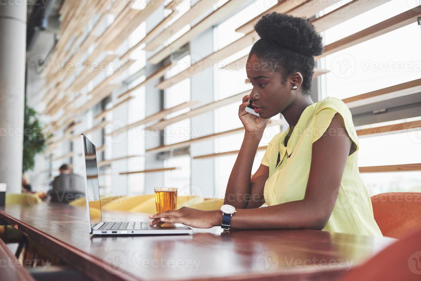 Joven y bella mujer de negocios afroamericana hablando por teléfono mientras trabajaba en un café foto