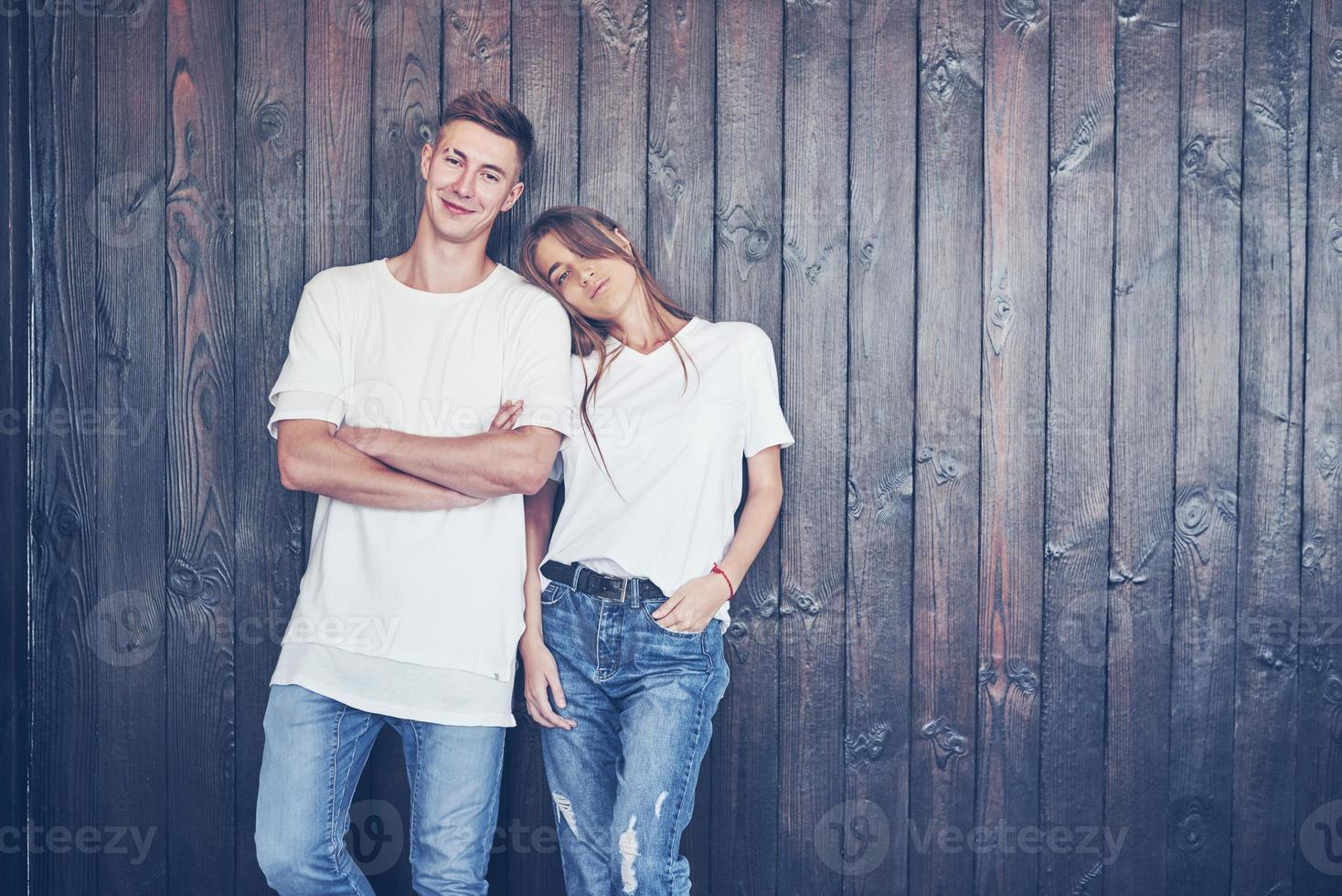 Young couple, guy and girl together on a wooden wall background. They are happy together and dressed alike. Always in a trend photo