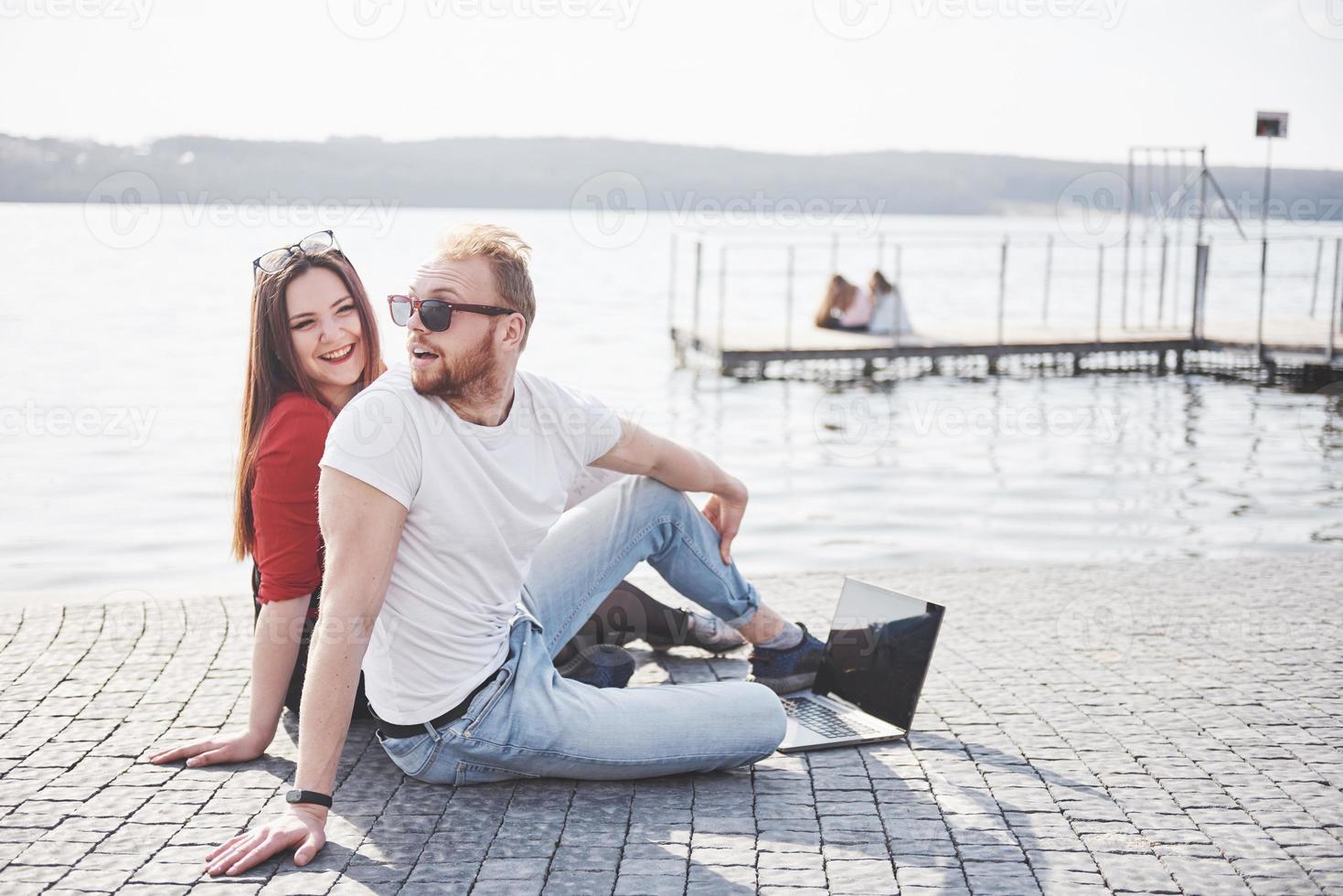 Dos estudiantes, chico y chica, están sentados al aire libre y disfrutando de una computadora portátil, estudiando al aire libre en un día soleado foto